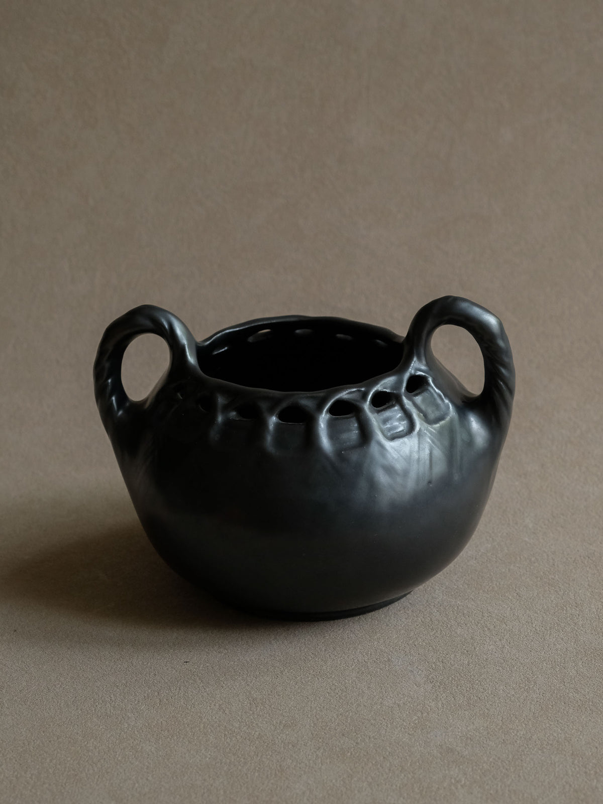 Early 20th-century black ceramic vase with twin loop handles, broad rounded body and dark satin metallic-looking glaze, front view.