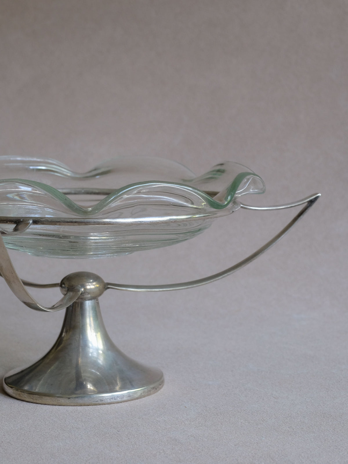 Angled view of the Art Deco EPNS and glass tazza showing the shallow clear bowl and open metal support.
