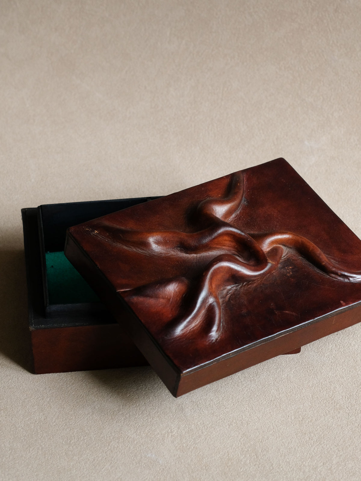 Angled view of the burgundy-red leather jewellery box showing the raised sculptural relief and slim rectangular profile.