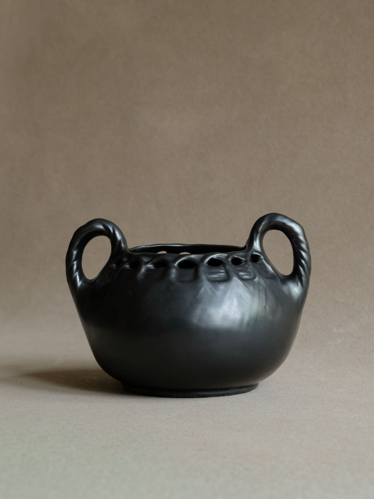 Straight-on view of an early 20th-century black ceramic vase with twin loop handles and deeply recessed decoration beneath the rim.