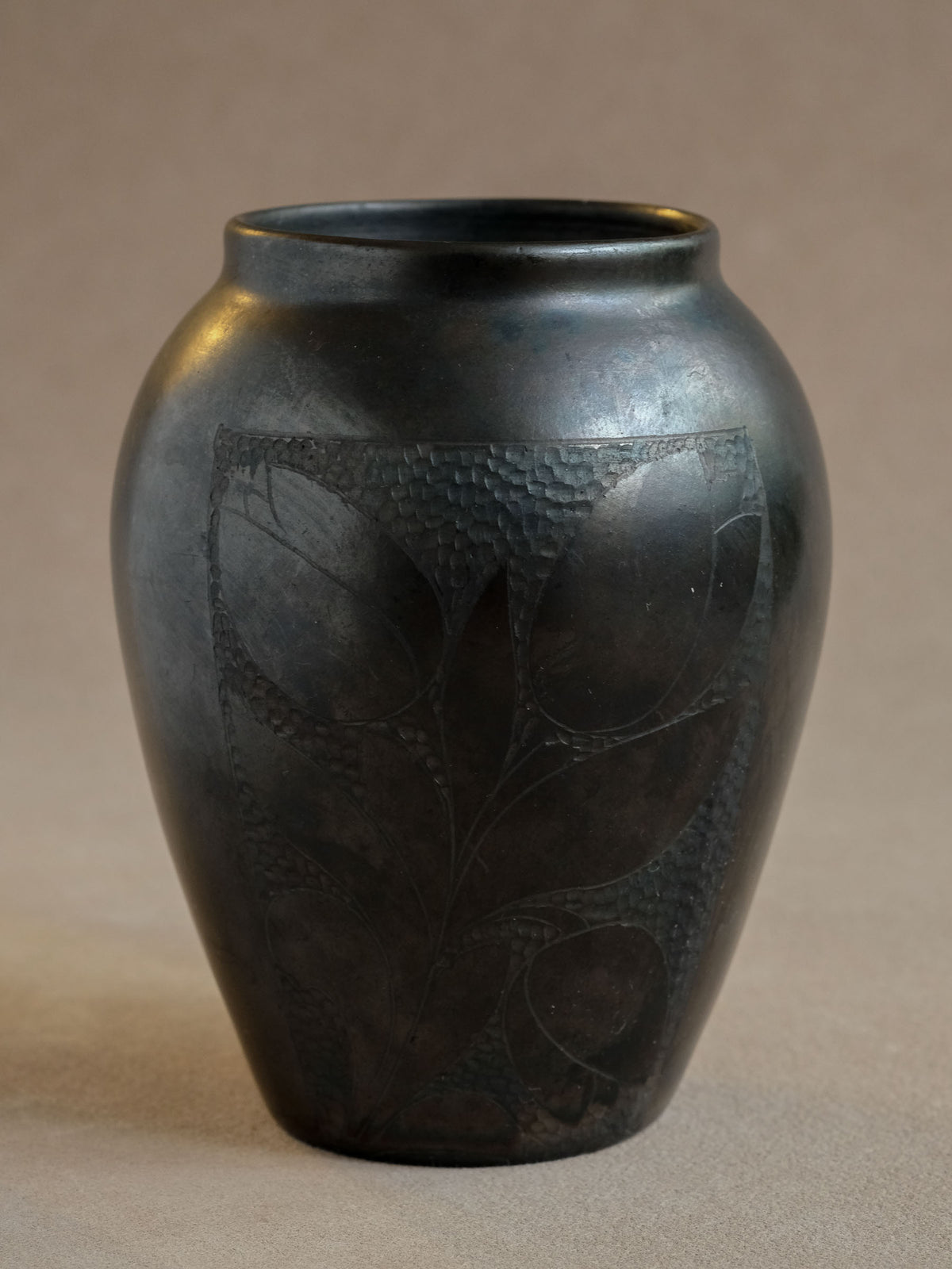 Detail view of the incised floral motif and subtle metallic, iridescent colour variation in the dark ceramic glaze.