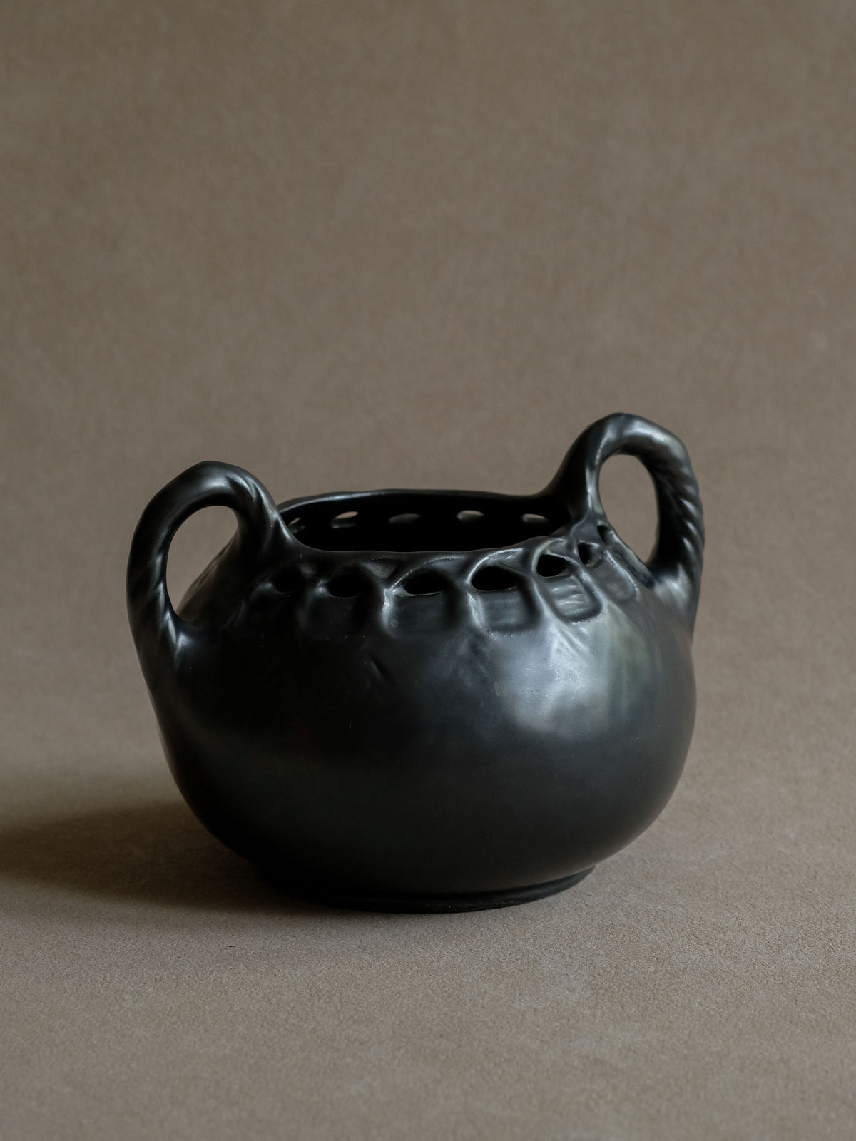 Three-quarter view of the sculptural black ceramic vase showing its rounded body, twin handles and metallic-looking satin glaze.