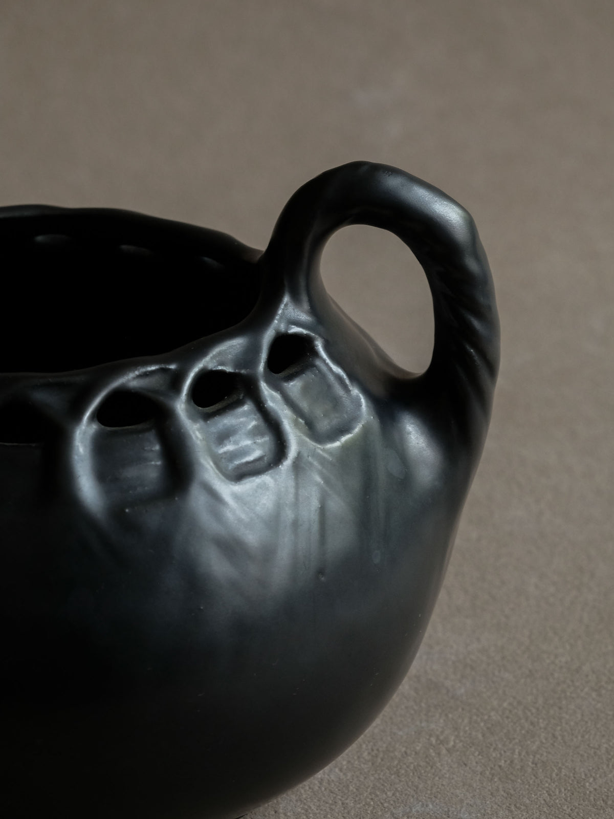 Detail of the recessed upper motif and dark metallic-looking glaze on the early 20th-century black ceramic vase.