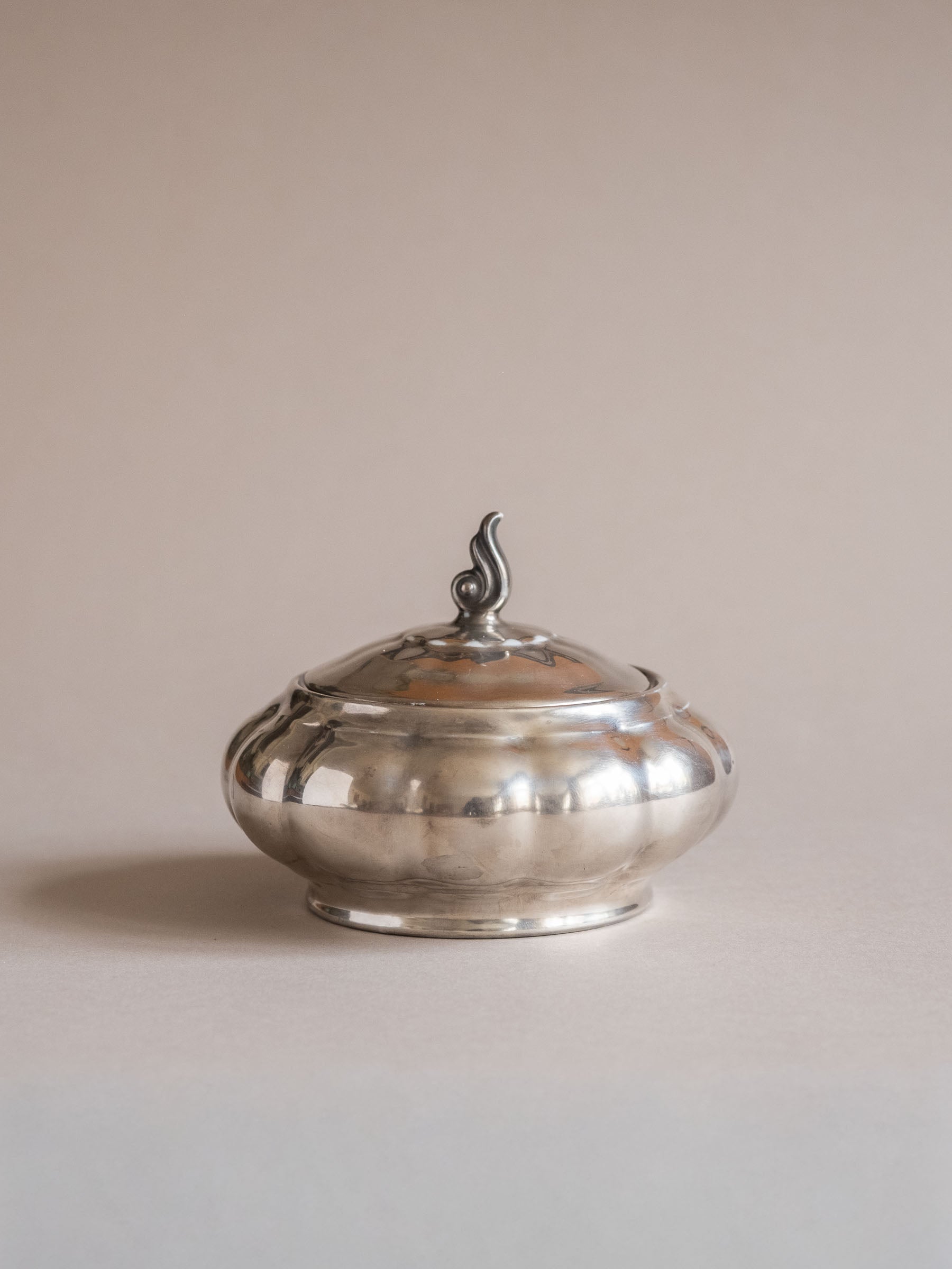 Front view of the silver-plated porcelain lidded sugar bowl, showing the lobed body and small curled finial.