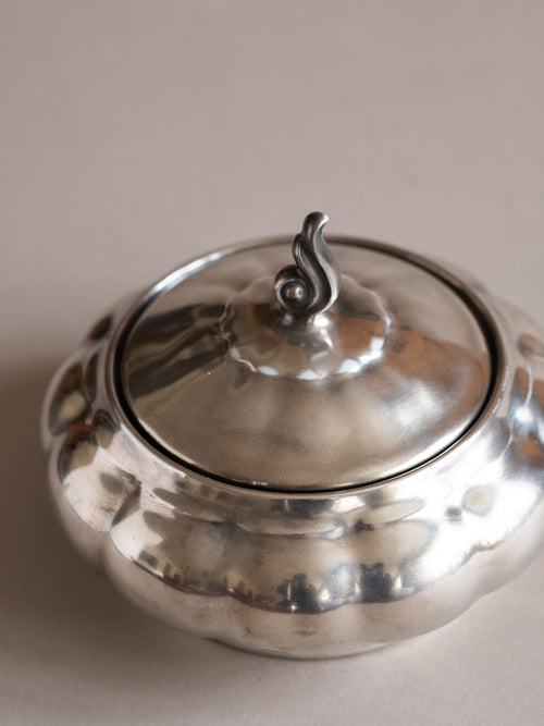 Close view of the silver-plated porcelain sugar bowl lid and upper body, showing the curled finial and soft reflective surface.
