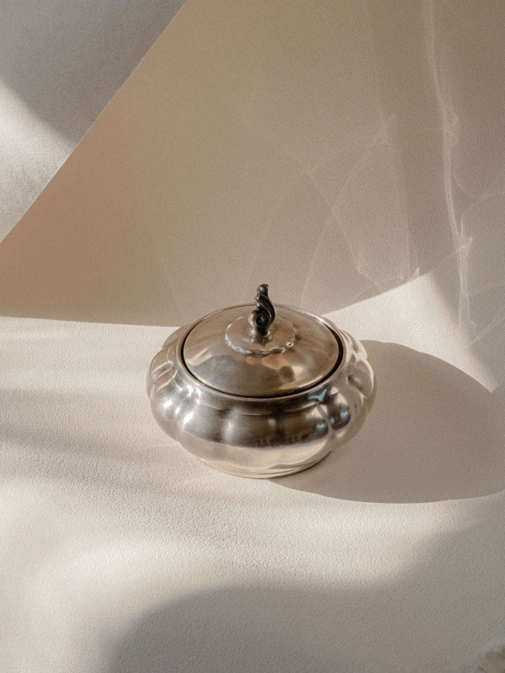 Three-quarter view of the silver-plated porcelain sugar bowl on a neutral background, with the lid closed.