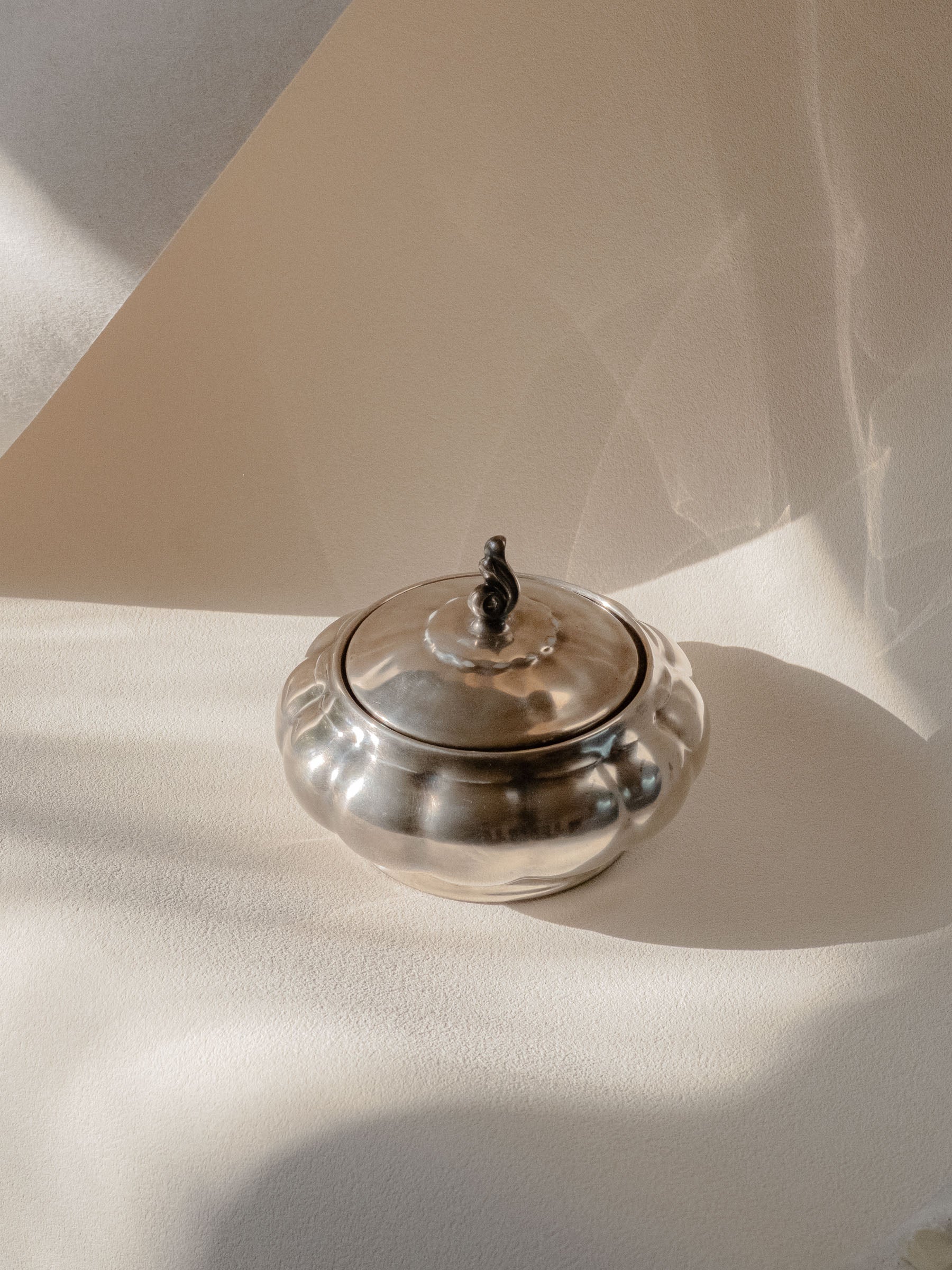 Three-quarter view of the silver-plated porcelain sugar bowl on a neutral background, with the lid closed.
