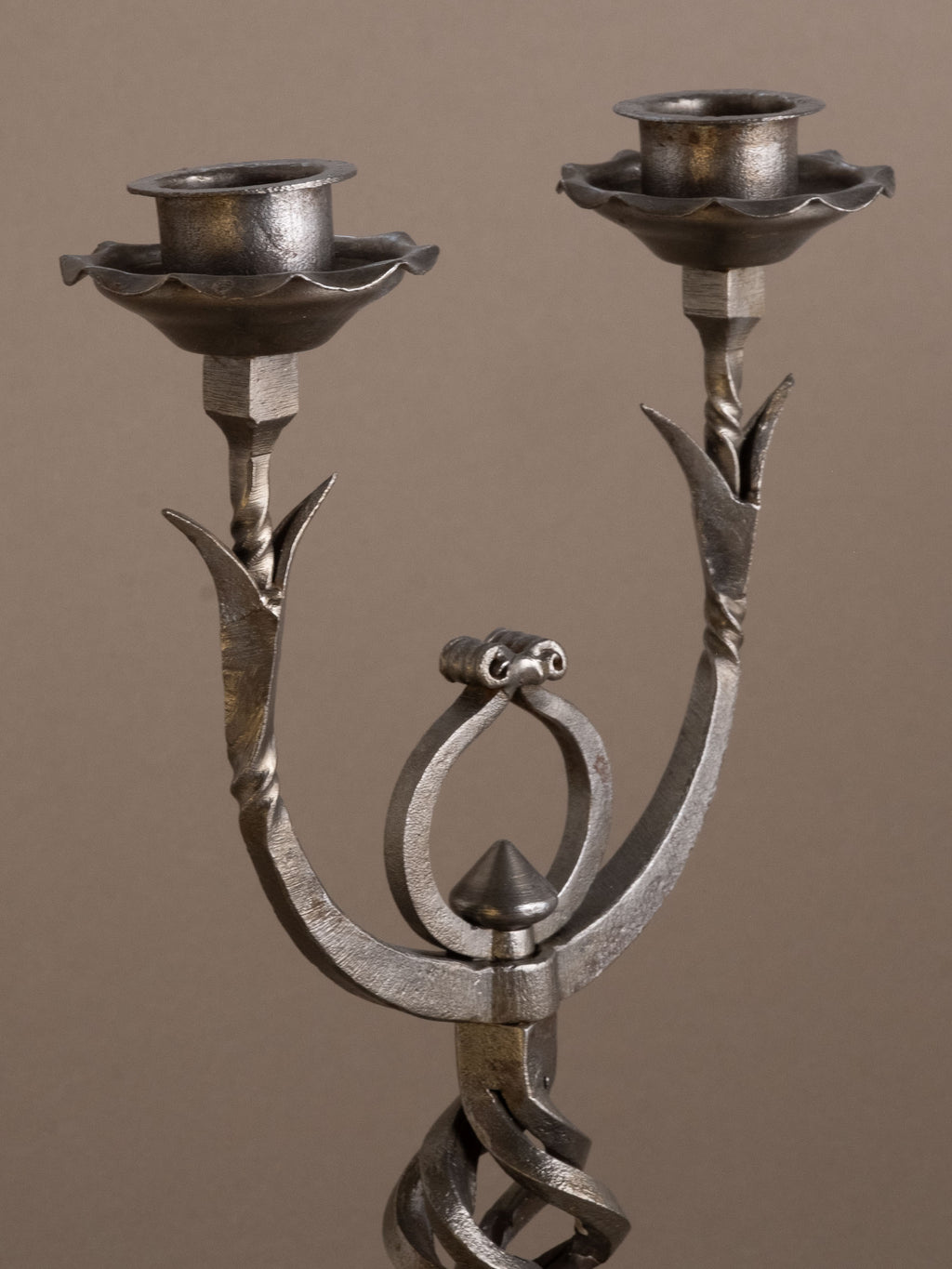 Three-quarter view of wrought iron two-arm candleholder with scroll arms and twisted stem.