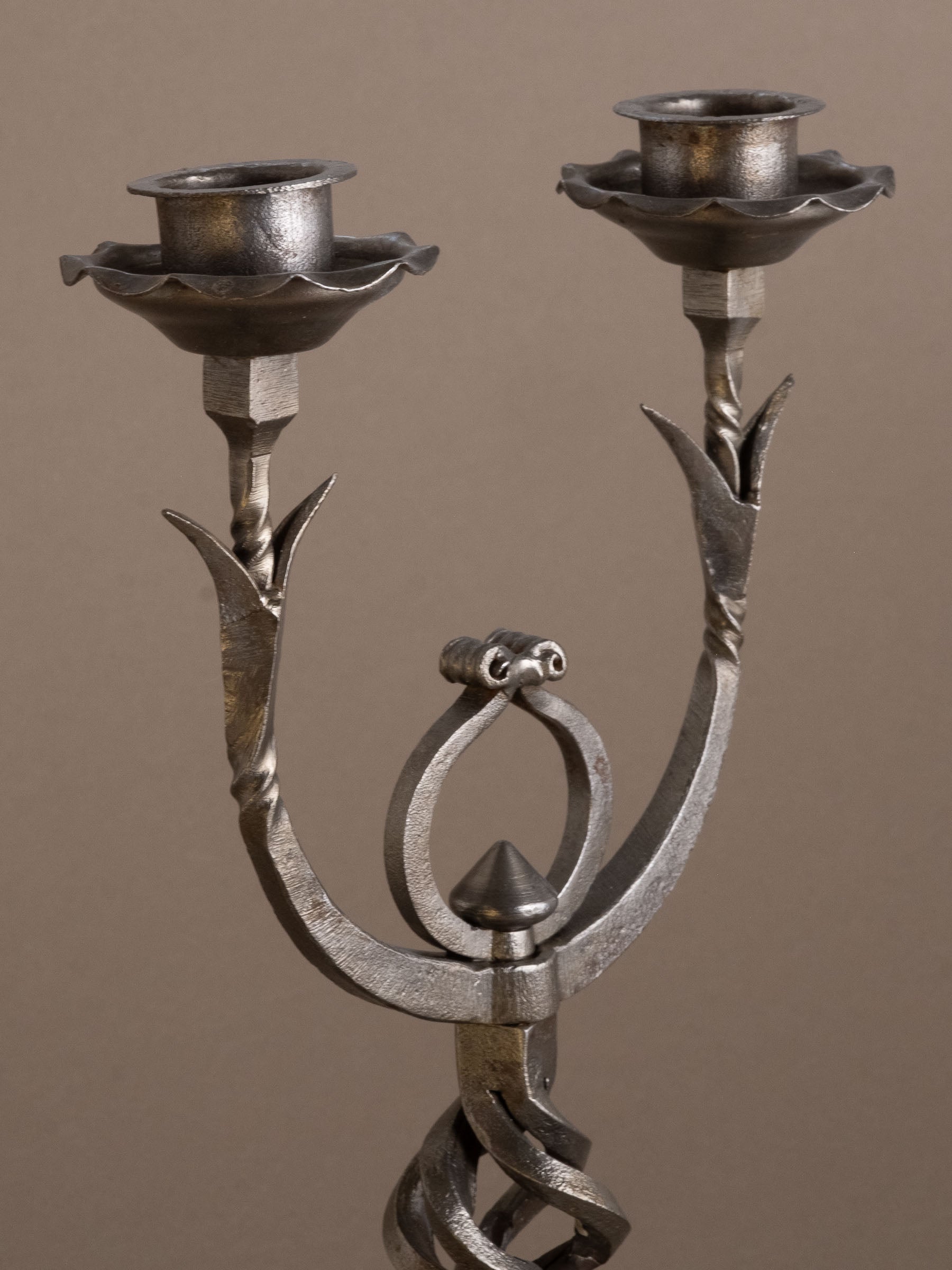 Three-quarter view of wrought iron two-arm candleholder with scroll arms and twisted stem.