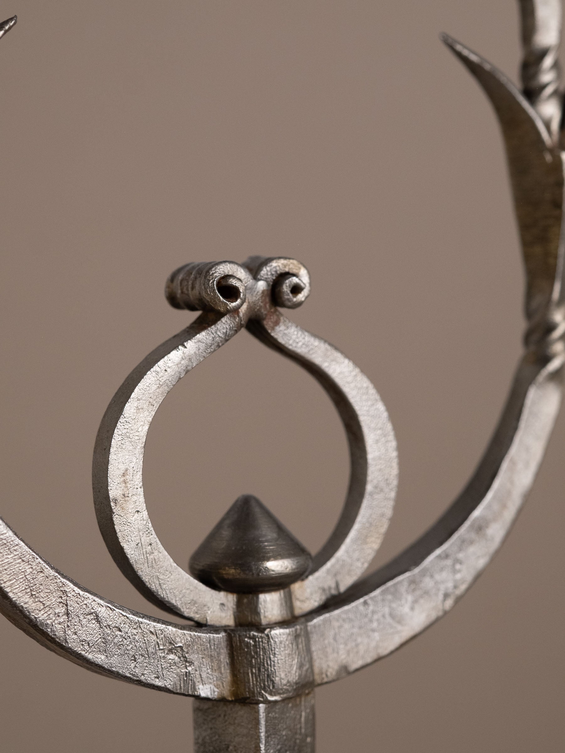Scroll element beneath arms of hand-forged wrought iron candleholder.