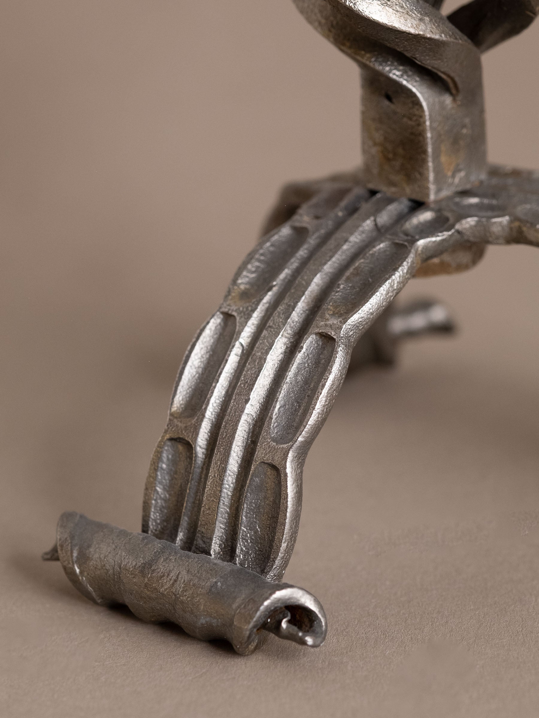 Close-up of foot on wrought iron two-arm candleholder showing hammered texture and curled terminal.