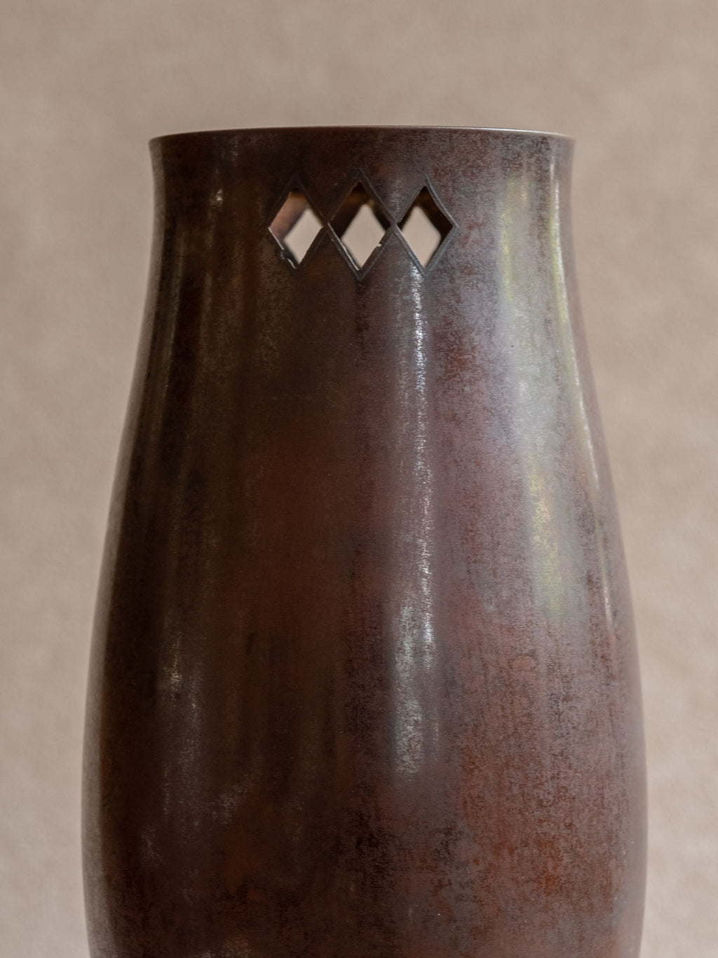 Close-up of a Japanese cast copper vase showing reddish-brown patina and small diamond openwork near the mouth.
