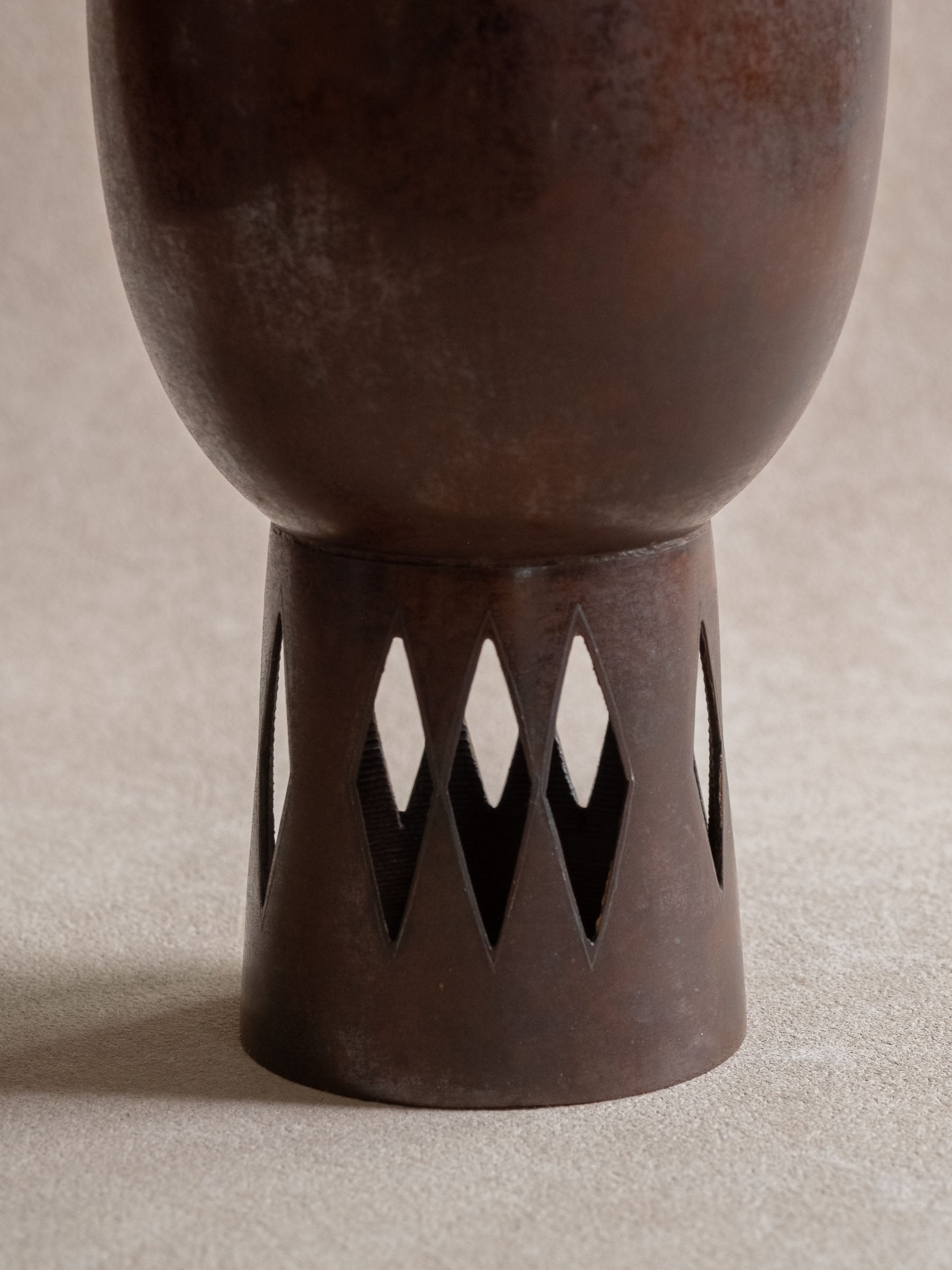 Close-up of the raised foot of a Japanese cast copper vase with repeated diamond-shaped openwork.
