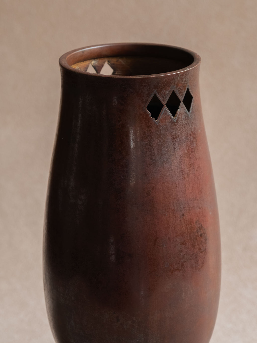 Close-up of the upper body of a Japanese cast copper vase showing dark patina and diamond-shaped openwork near the rim.
