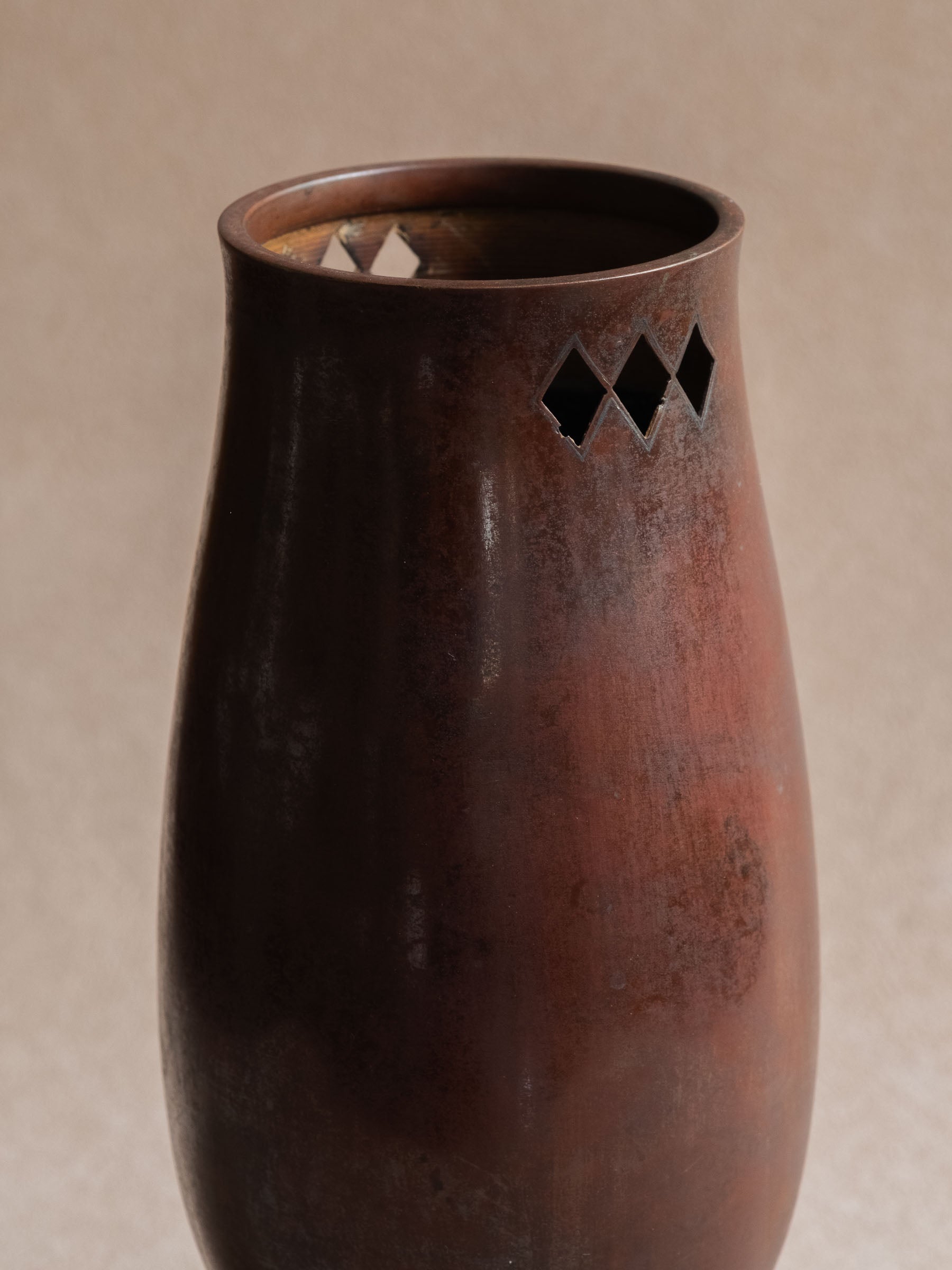 Close-up of the upper body of a Japanese cast copper vase showing dark patina and diamond-shaped openwork near the rim.
