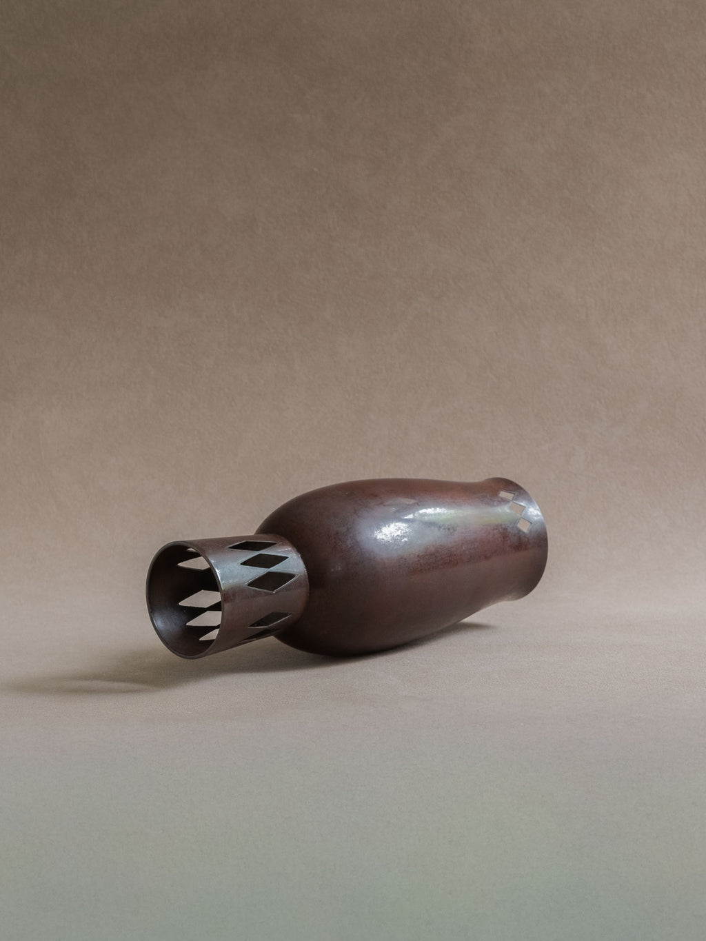 Side view of a Japanese cast copper vase lying down, showing the openwork foot and rounded body.
