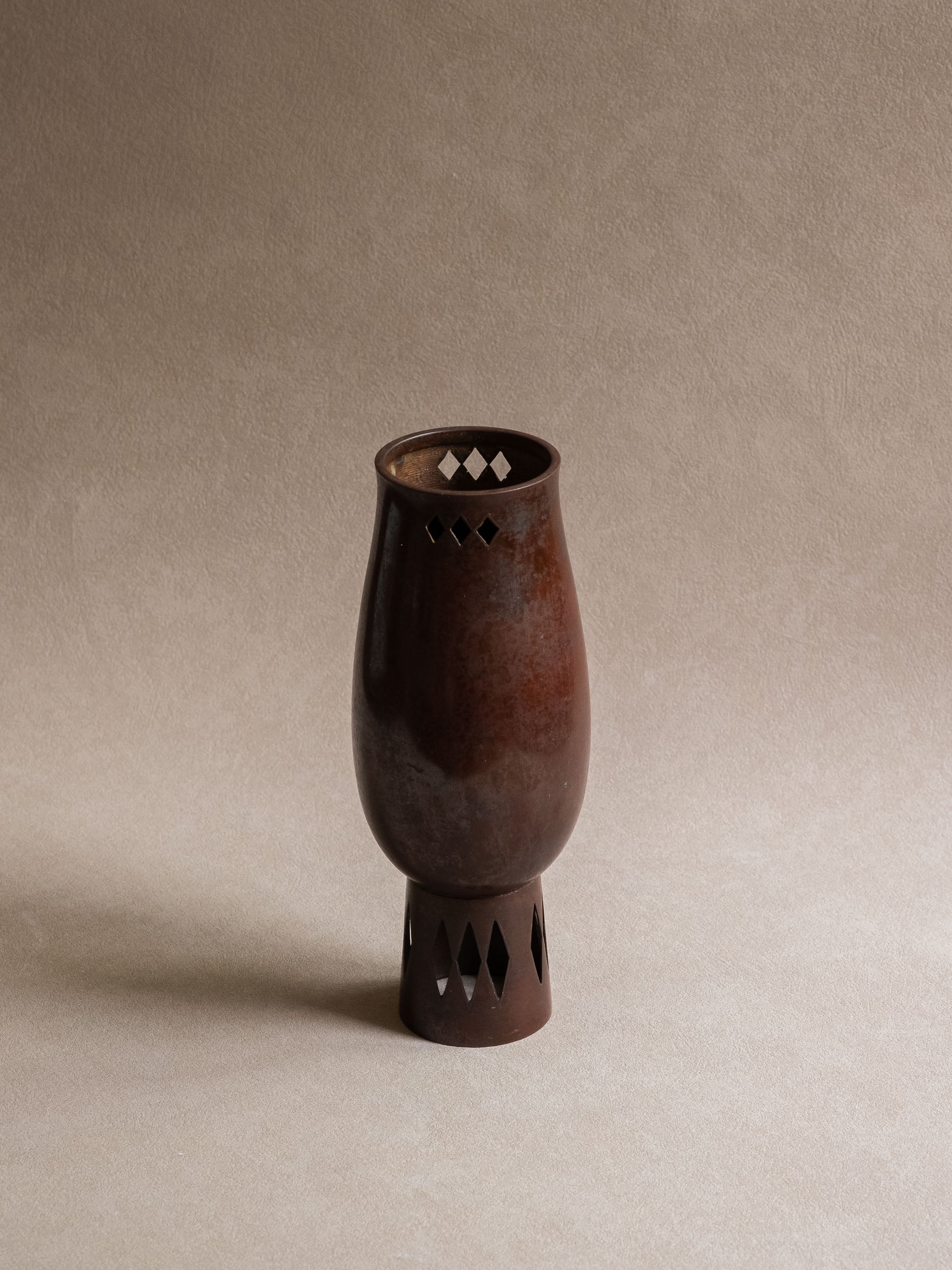 Full view of a Japanese Takaoka cast copper vase with elongated body, narrow mouth, and pierced geometric foot.
