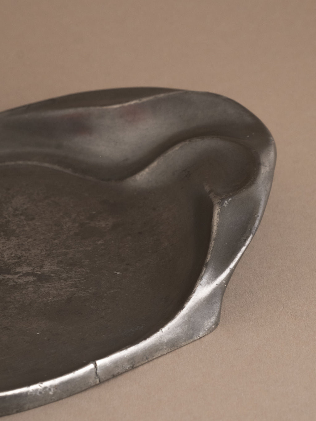 Close-up of asymmetrical rim on Kayserzinn art pewter plate showing surface wear and hairline crack.