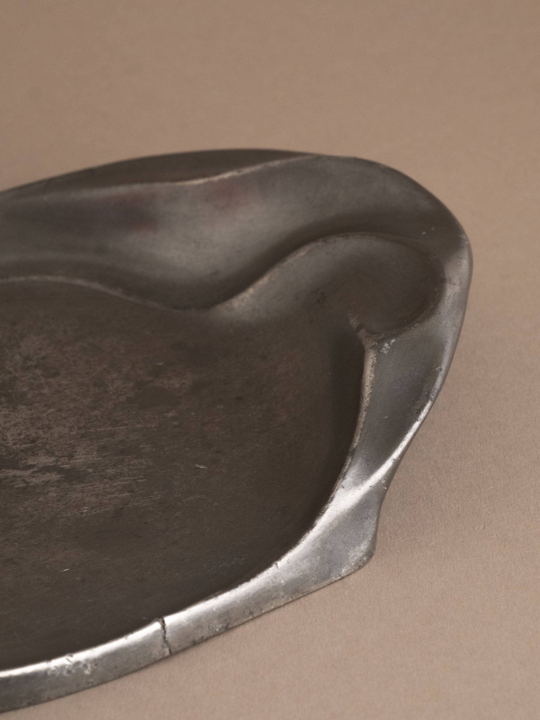 Close-up of asymmetrical rim on Kayserzinn art pewter plate showing surface wear and hairline crack.