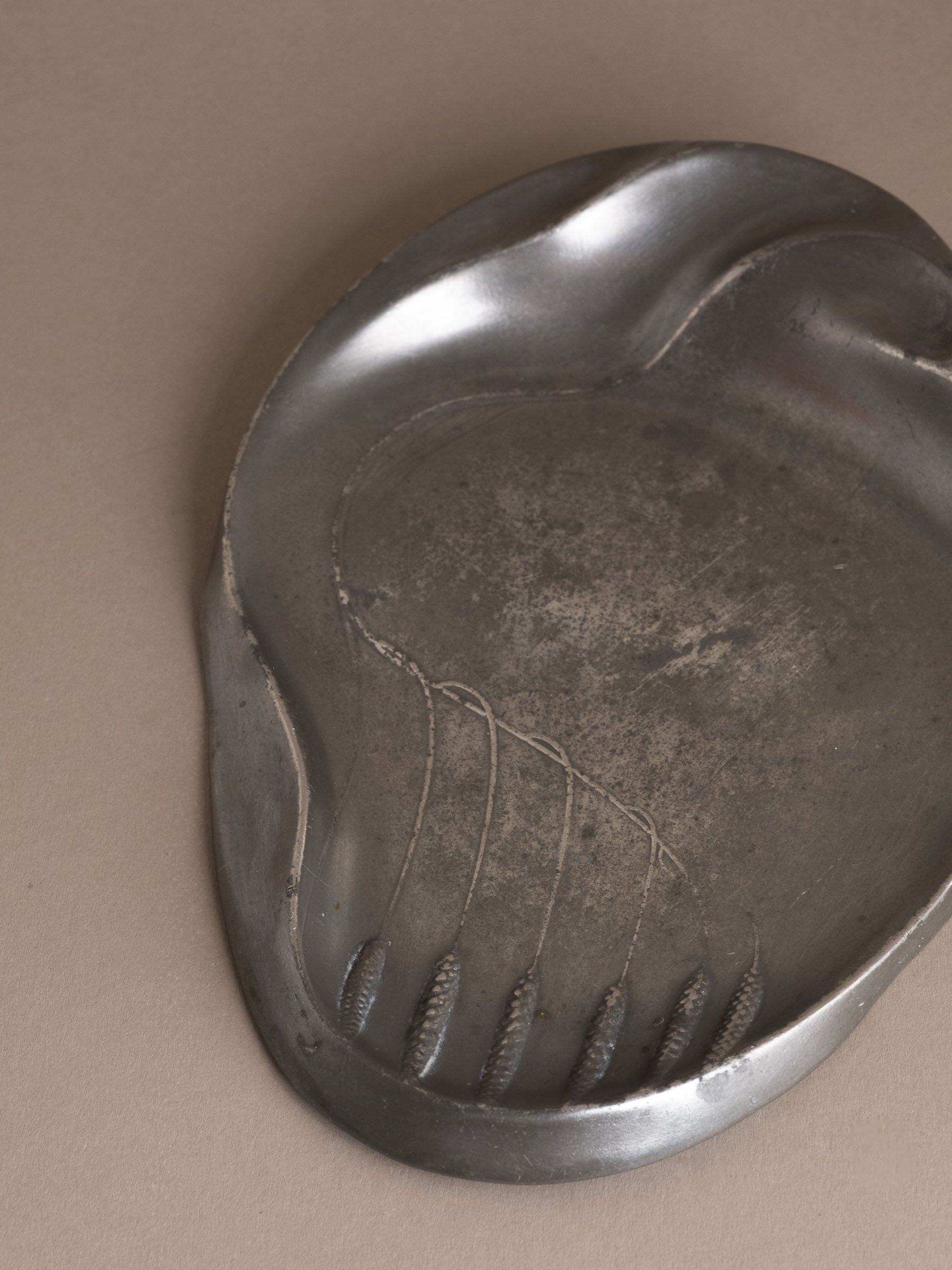 Close-up of wheat motif detail on Kayserzinn art pewter plate with textured matte surface.