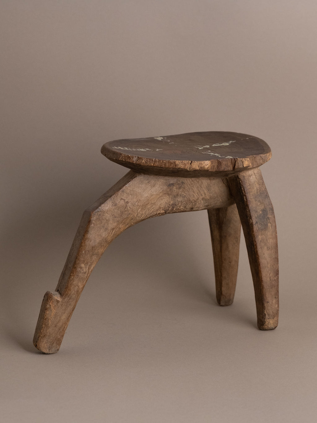 Angle view of carved wood Lobi stool showing three-leg construction and aged patina.