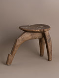 Angle view of carved wood Lobi stool showing three-leg construction and aged patina.
