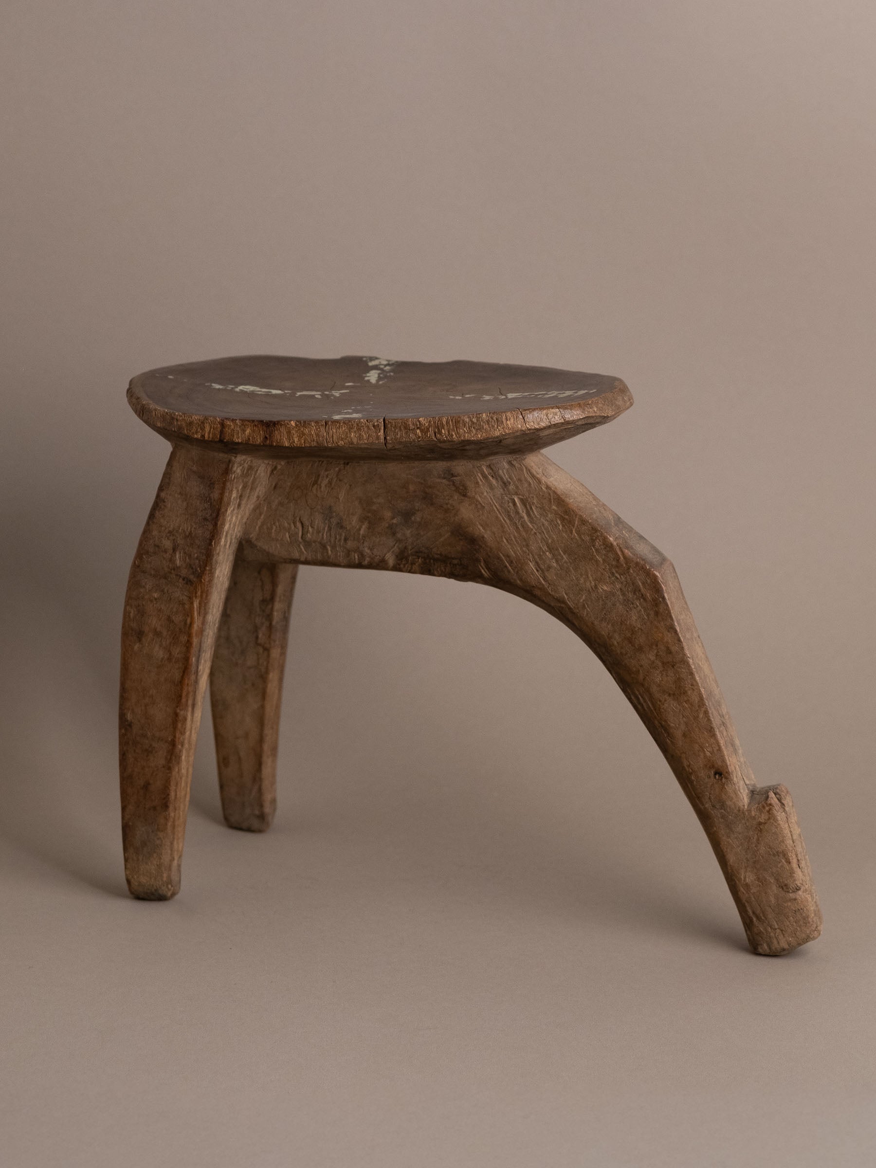 Full view of hand-carved wooden Lobi stool with three legs and sculptural curved front leg.