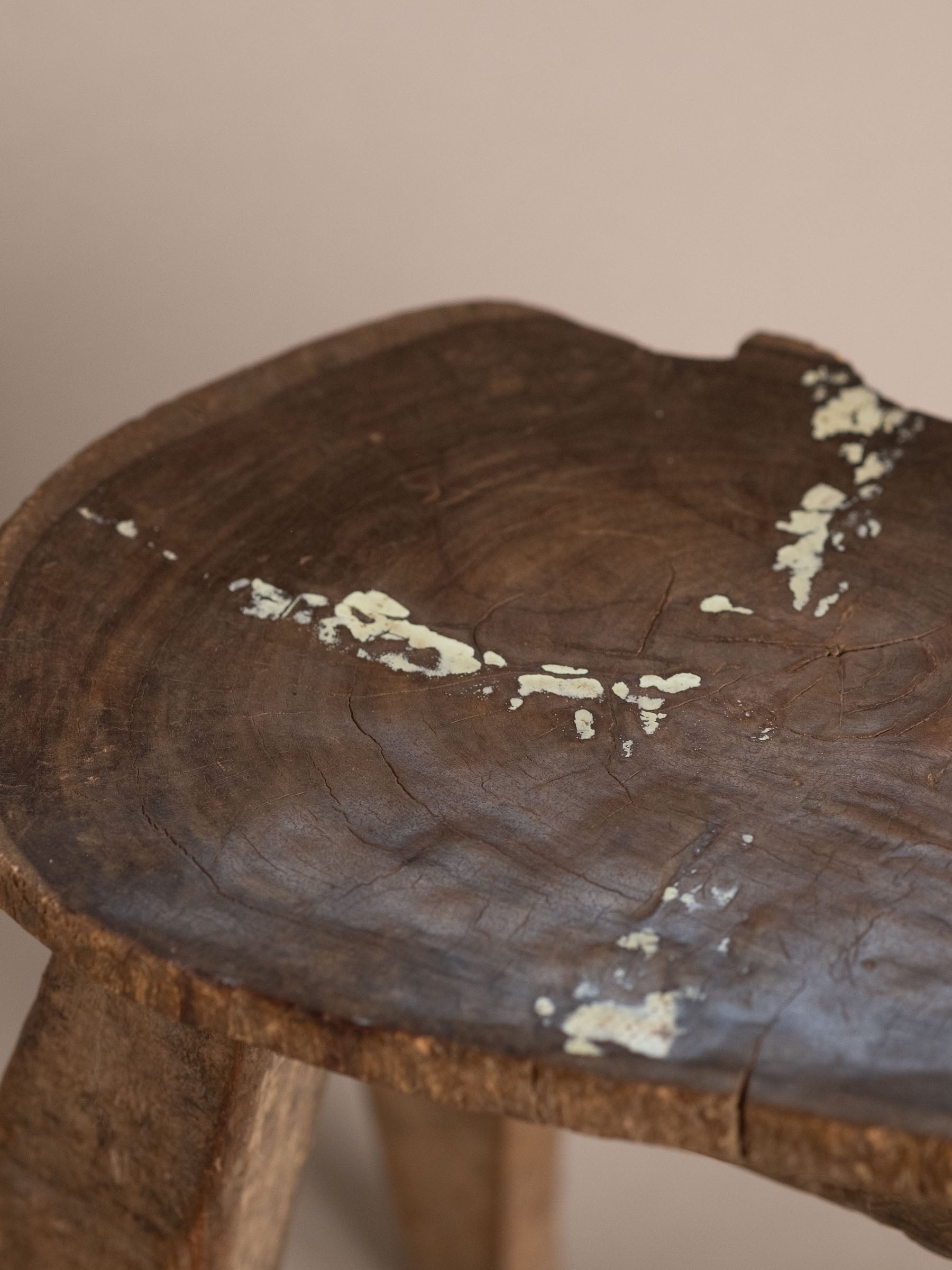 Top view detail of Lobi carved wood stool seat showing circular grain, natural cracks, and worn pale surface marks.