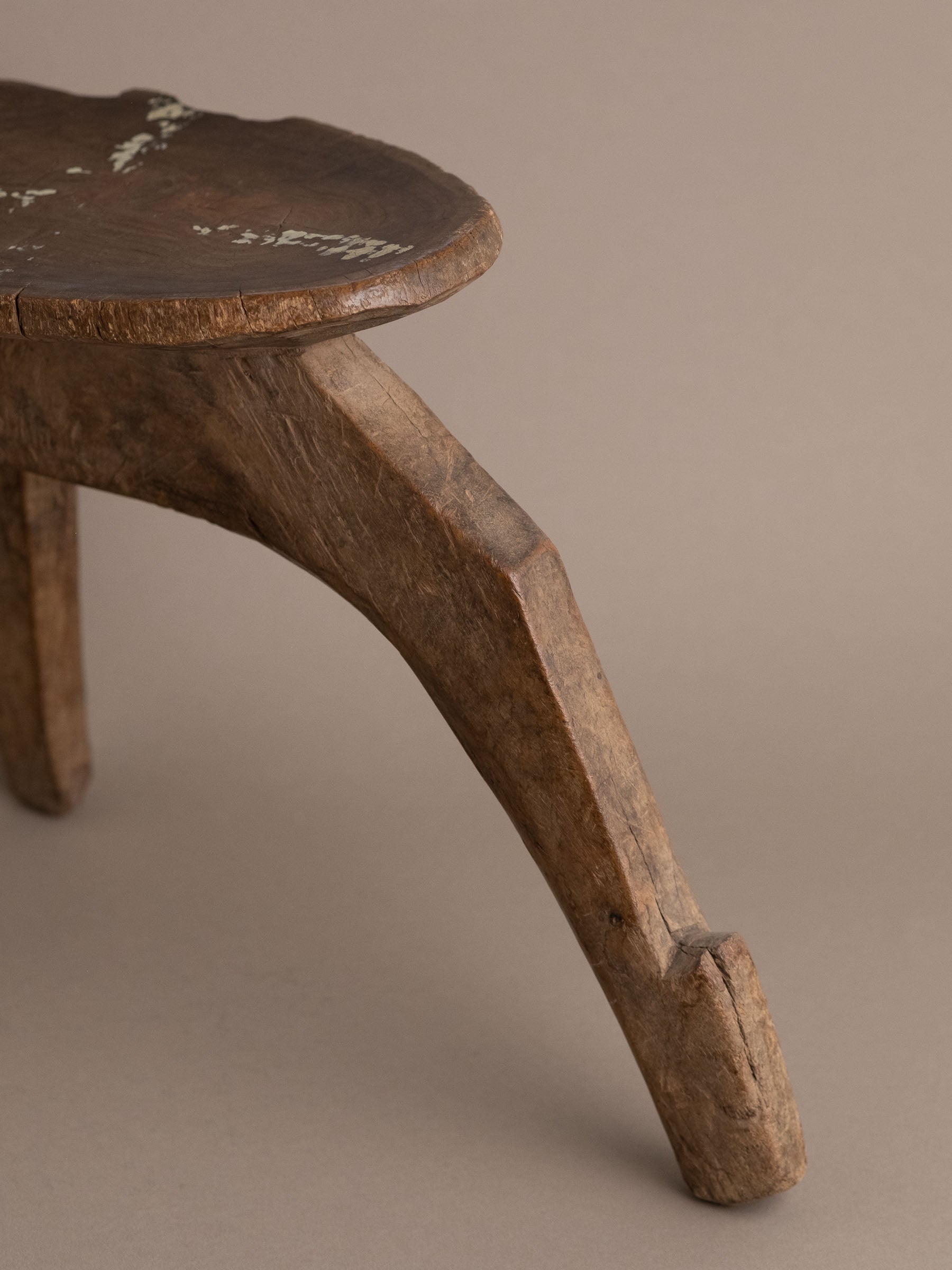 Close-up of a carved wood Lobi stool showing three-leg construction and aged patina.