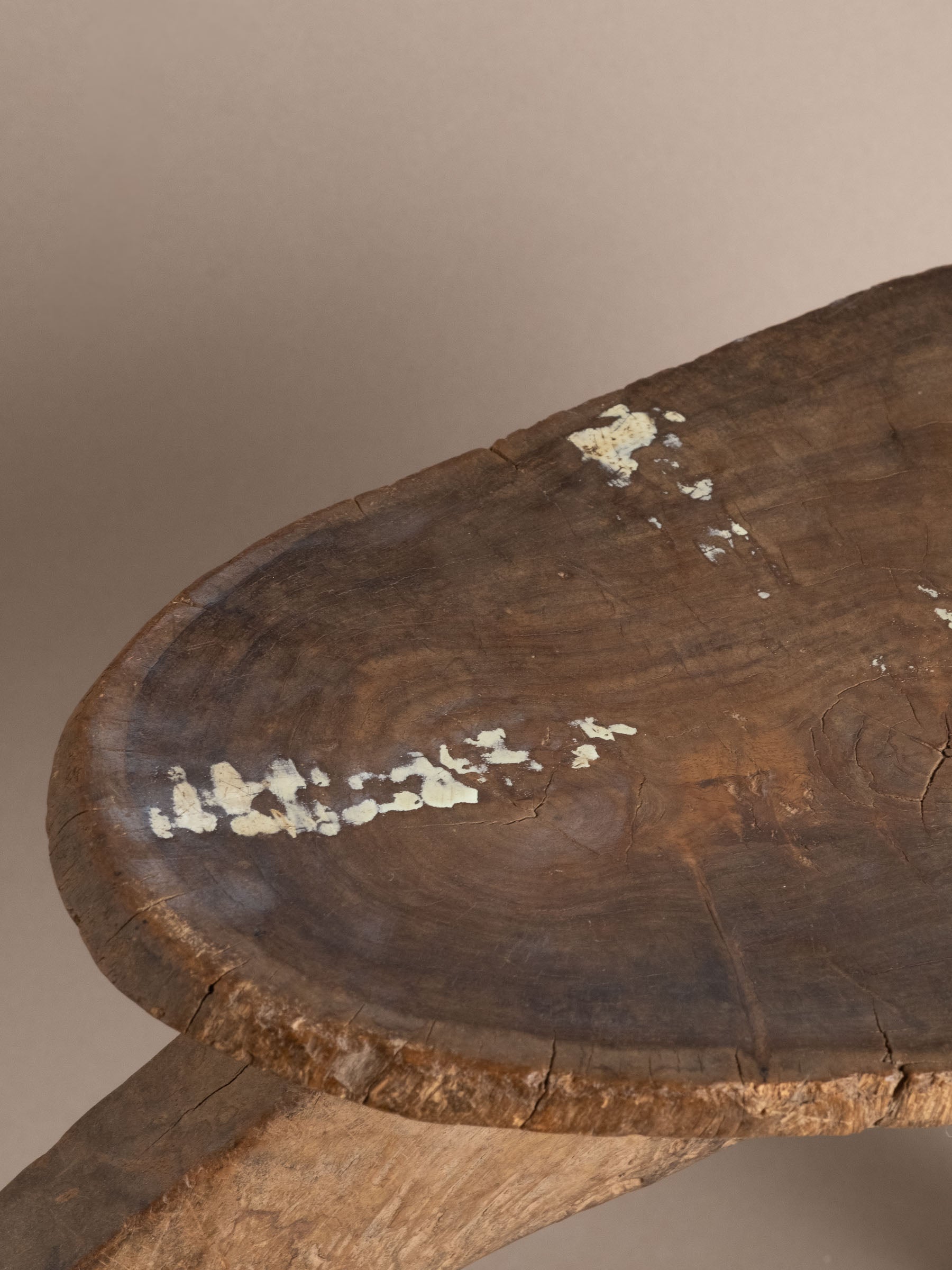 Close-up of carved wood Lobi stool seat showing circular grain, surface cracks, and worn pale areas.