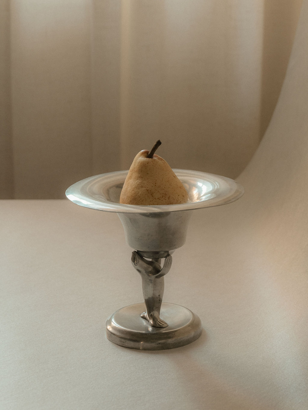 Pewter sea lion pedestal bowl by Dahlströms Tenn, Sweden, c. 1930s, shown holding a pear.
