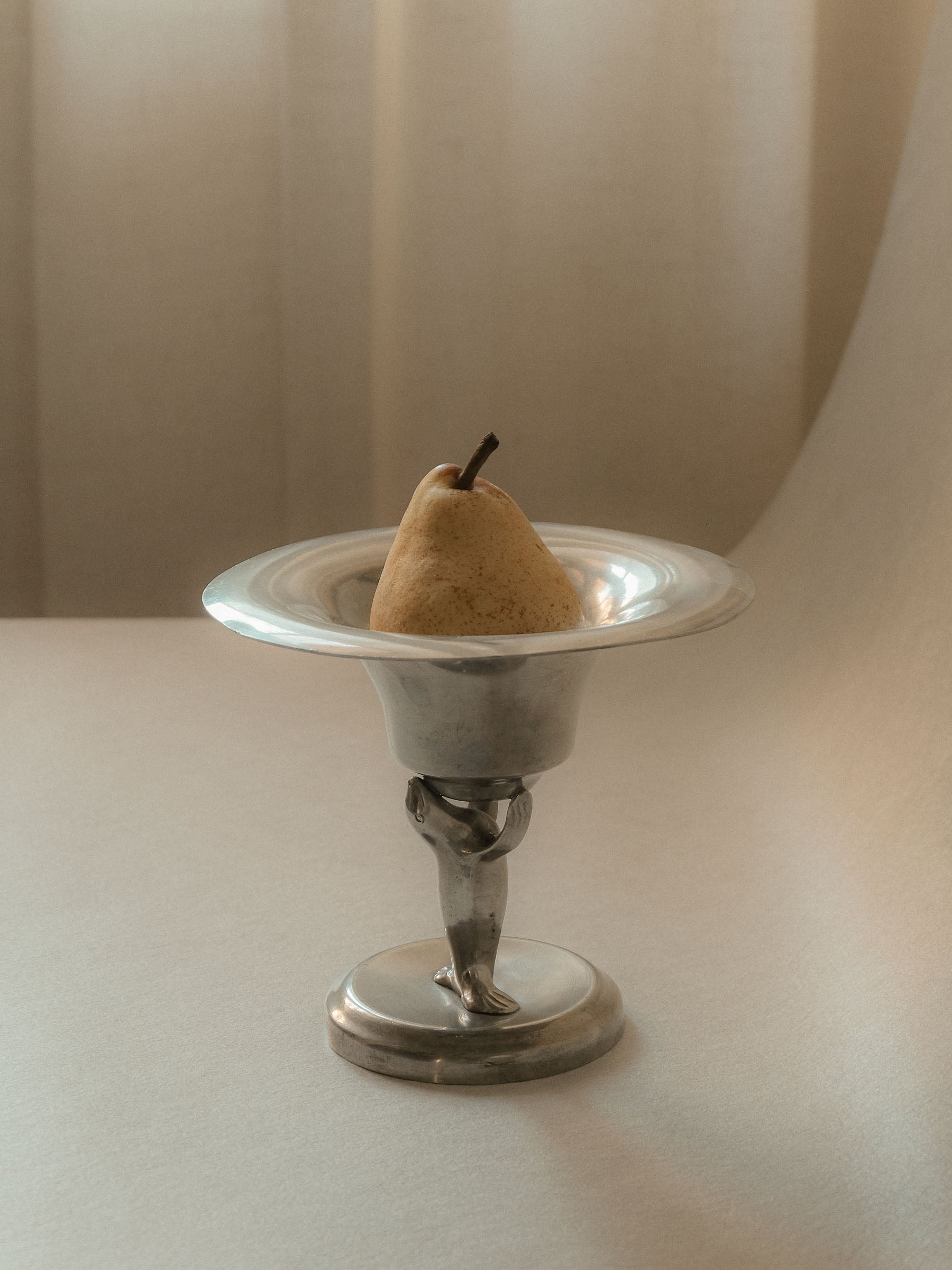 Pewter sea lion pedestal bowl by Dahlströms Tenn, Sweden, c. 1930s, shown holding a pear.