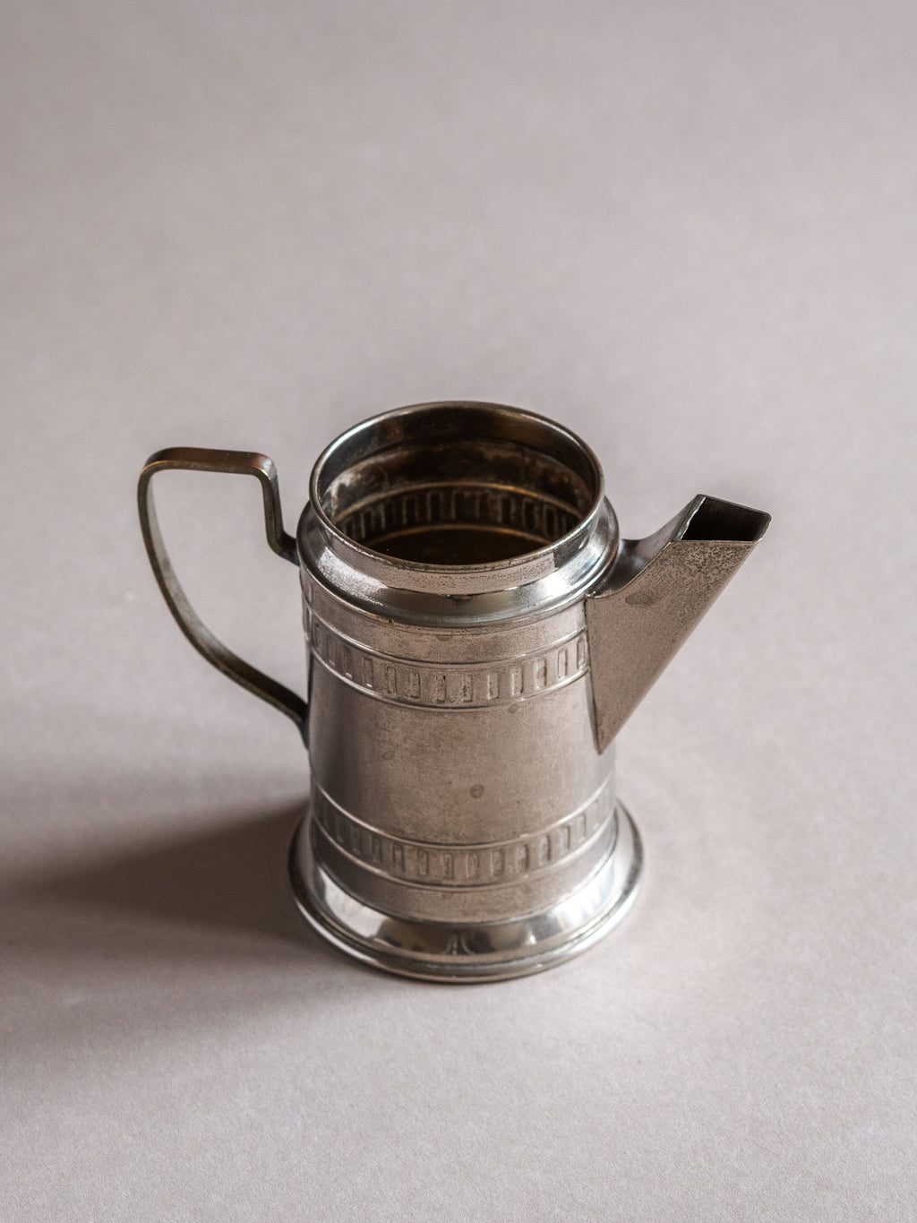 Small silver-plated cream jug shown against a pale background, with visible surface wear, open top, and slender handle.