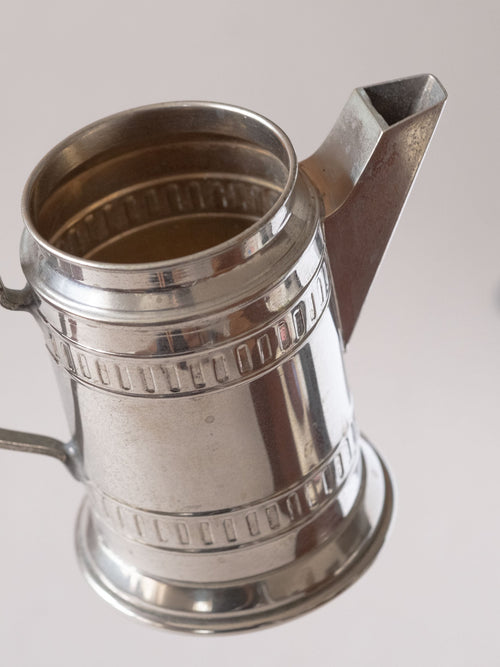 Close-up view of the upper section of a silver-plated cream jug, focusing on the angular spout, open rim, and geometric band decoration.
