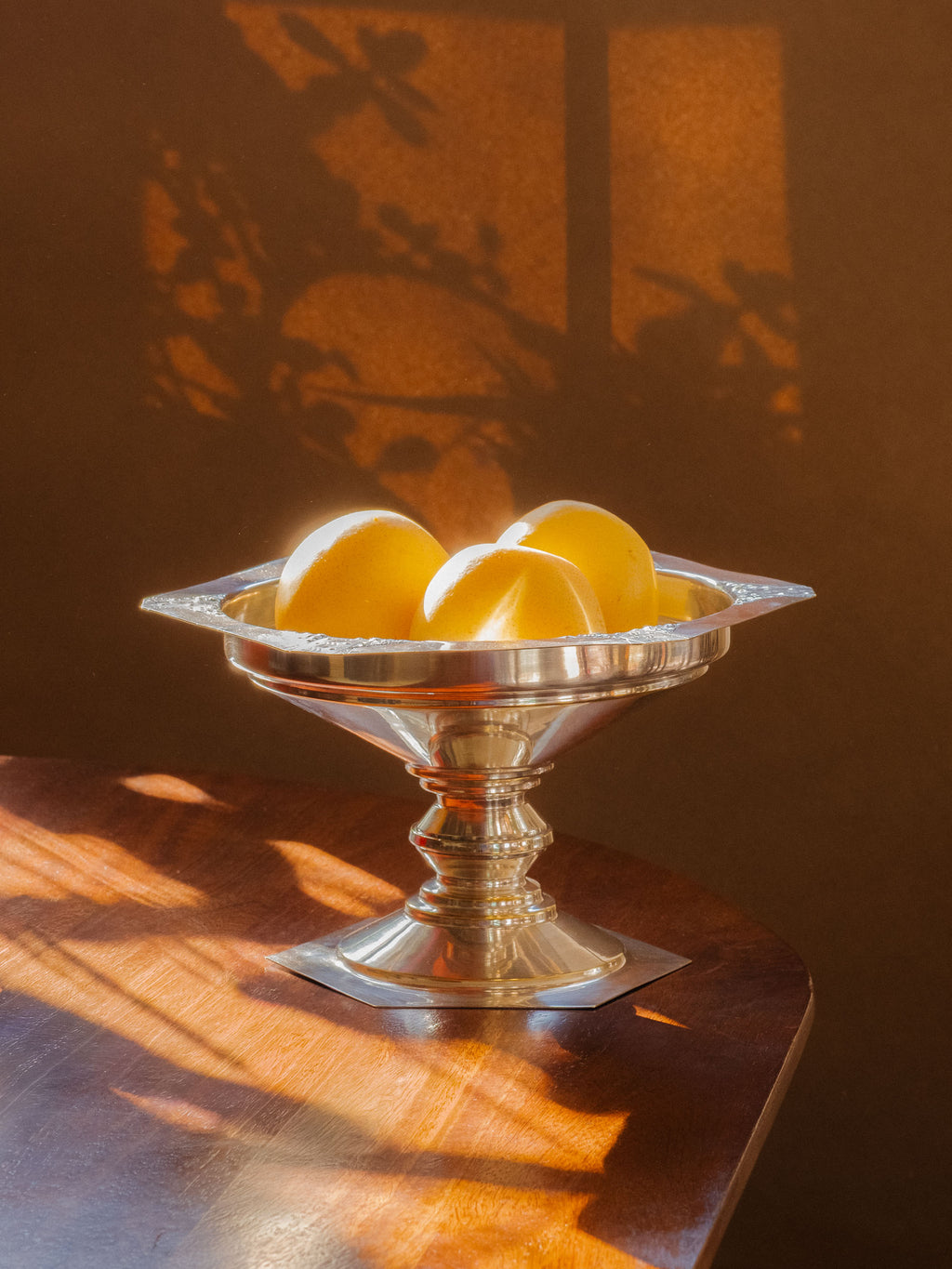 Art Deco silver-plated pedestal bowl styled with pears on a wooden table in strong natural light.