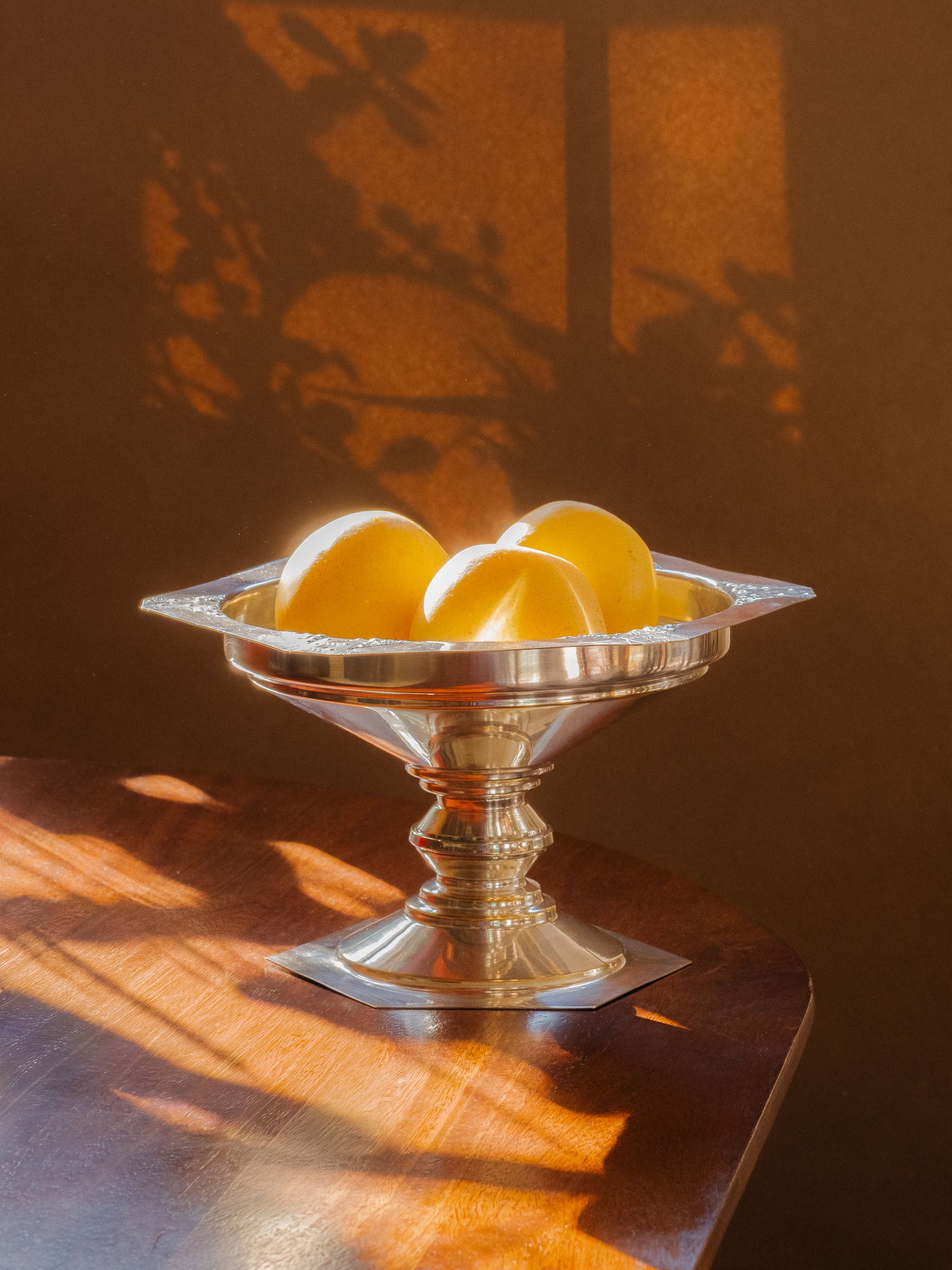 Art Deco silver-plated pedestal bowl styled with pears on a wooden table in strong natural light.