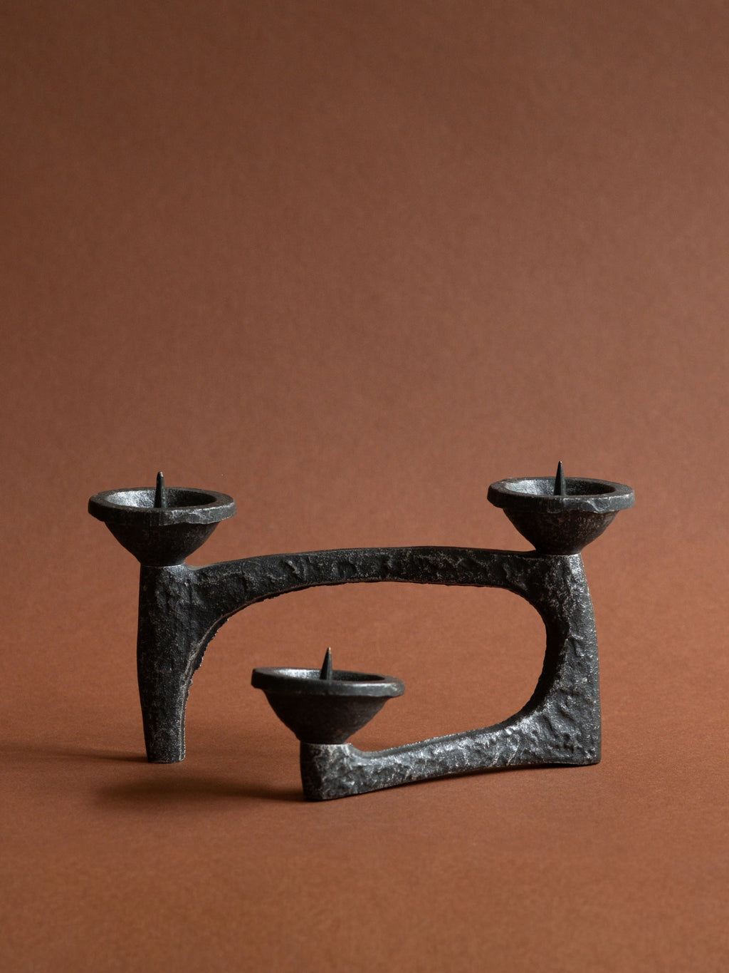 Full view of a low Brutalist cast iron three-light candleholder with looping architectural form and three pricket bowls.