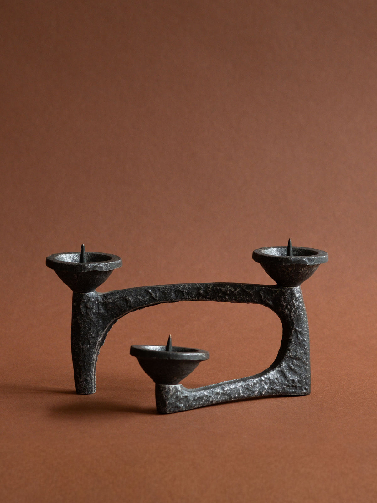 Full view of a low Brutalist cast iron three-light candleholder with looping architectural form and three pricket bowls.