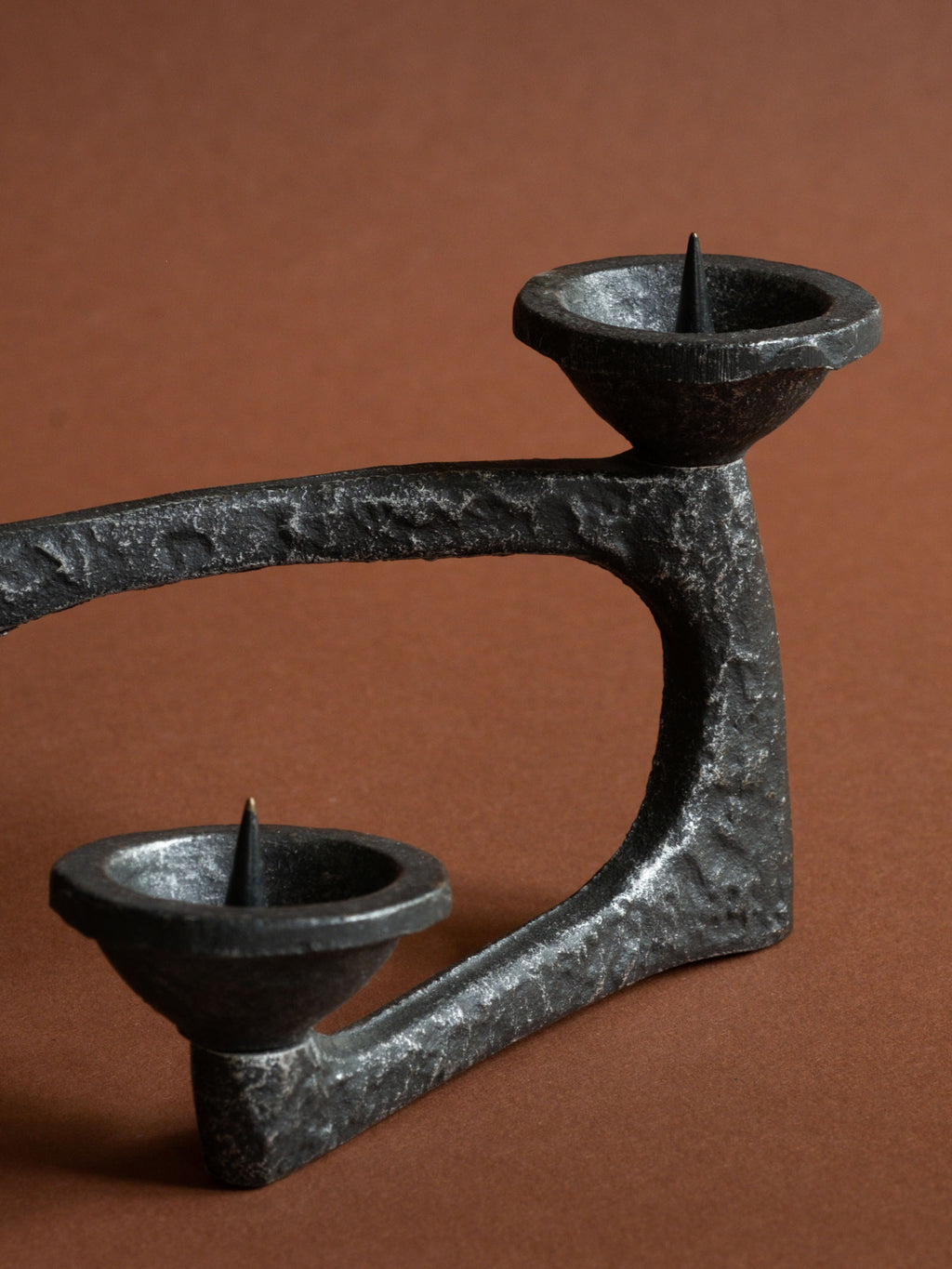Three-quarter detail of the cast iron candleholder showing its open loop, stepped candle bowls and rough surface.
