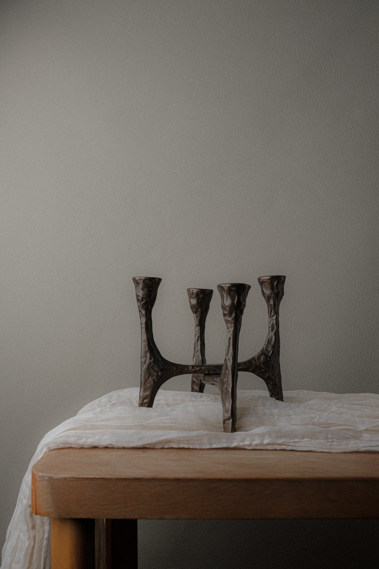 Brutalist four-arm bronze candleholder, Germany, 1970s, placed on a wooden table against a neutral wall.