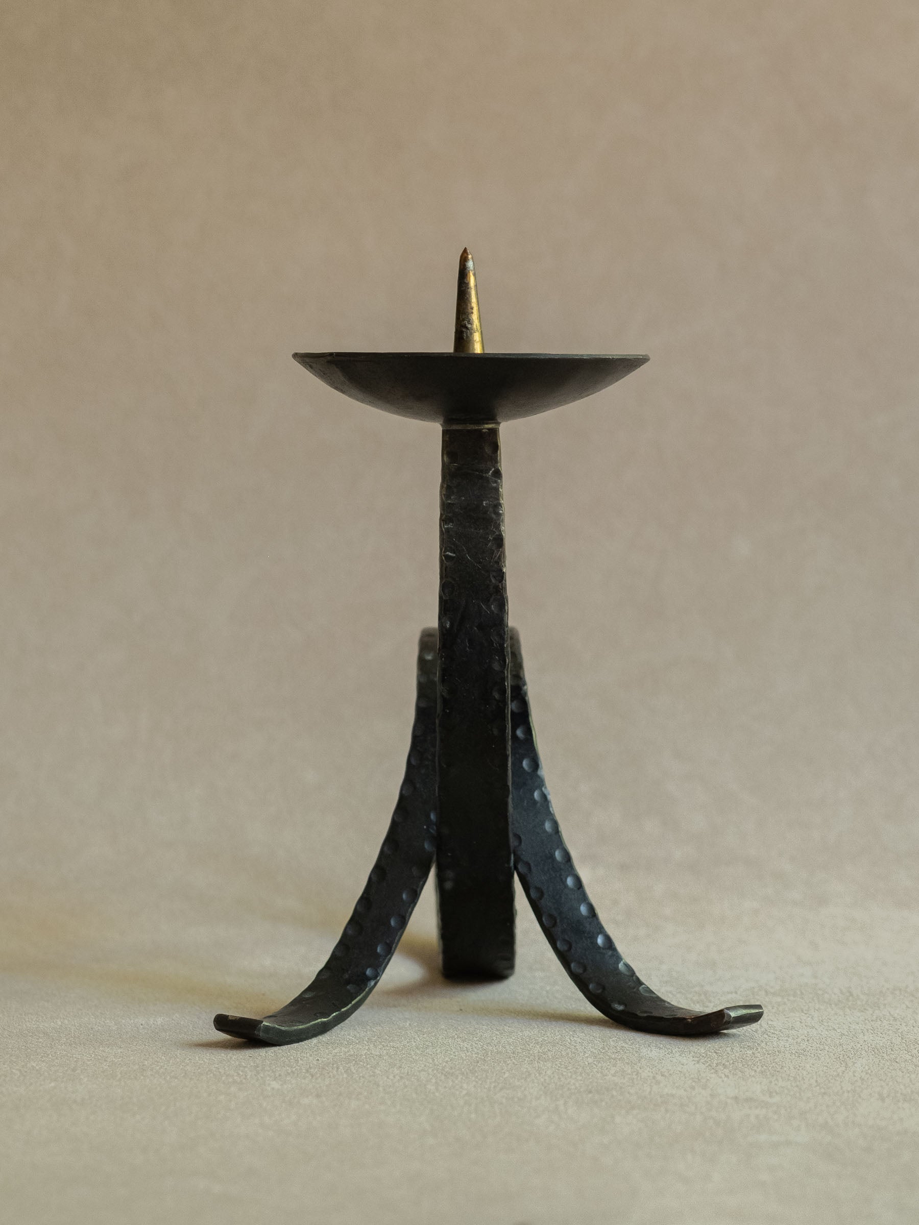 Rear view of the wrought iron pricket candleholder showing the vertical support, curved feet, punched-dot detail, and shallow drip pan.