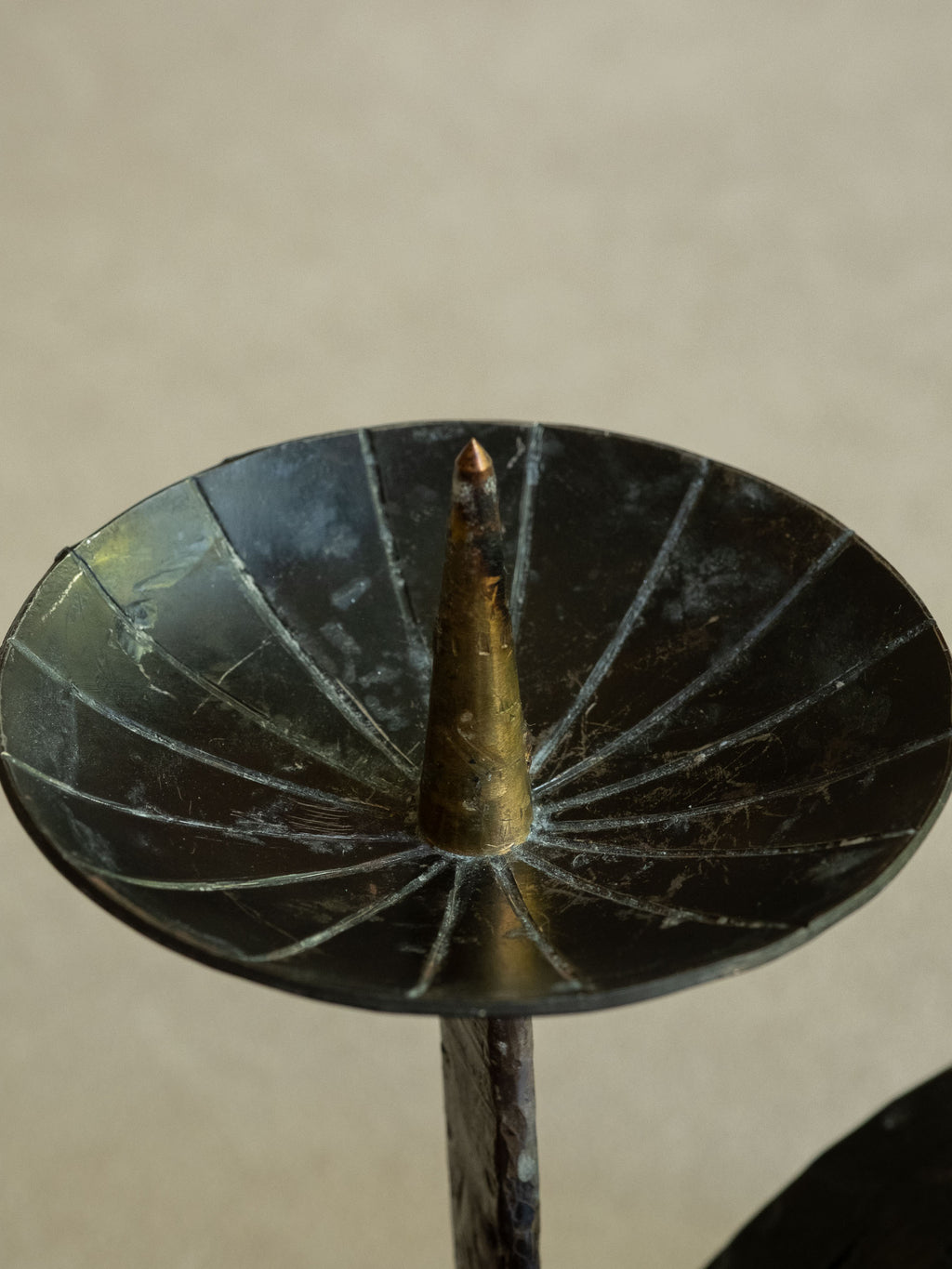 Close-up of the candleholder top showing the brass-toned central pricket, radial lines, scratches, and dark patinated drip pan.