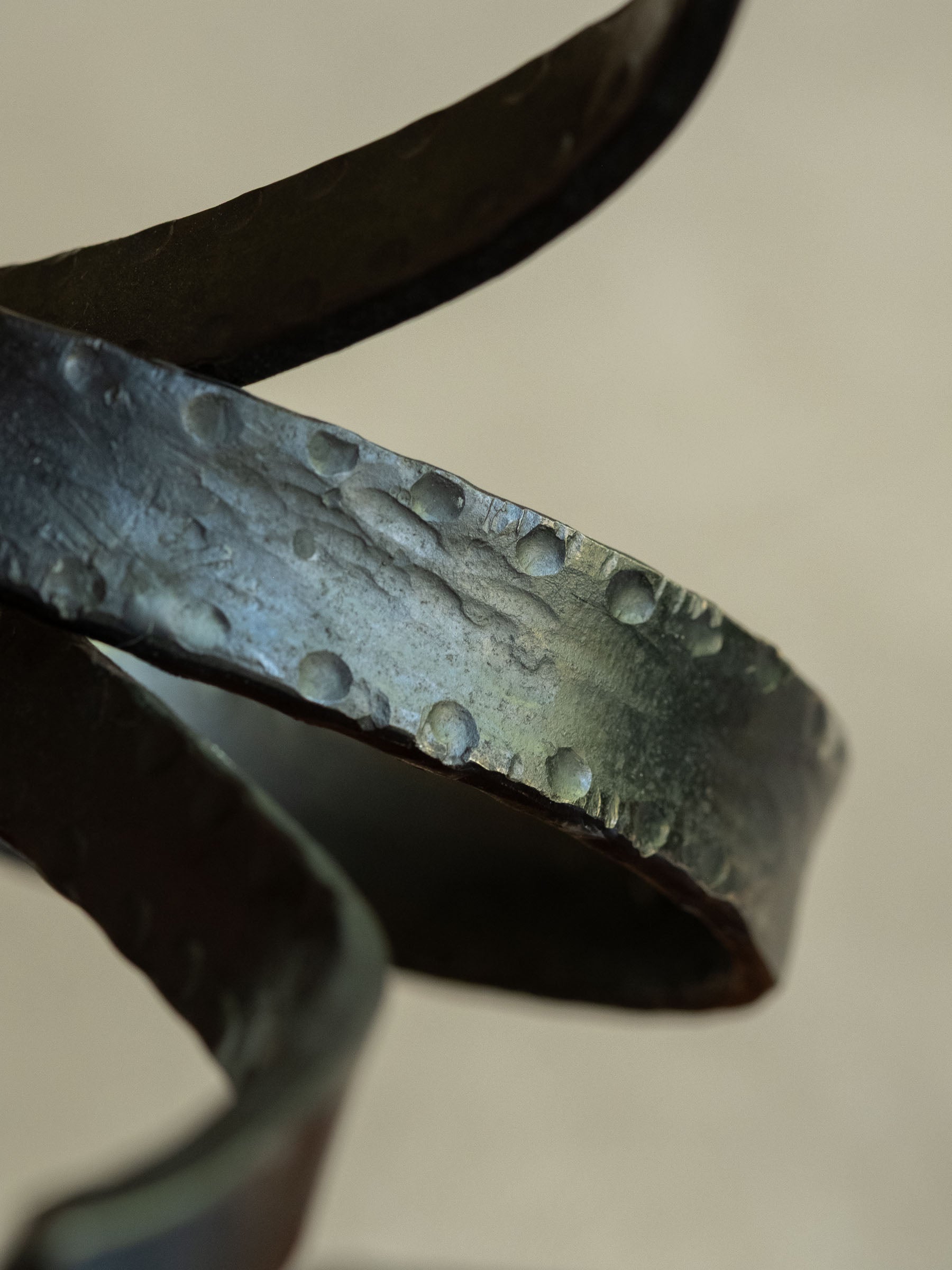 Close-up detail of the wrought iron loop showing punched-dot decoration, hammered texture, rubbed edges, and aged dark patina.