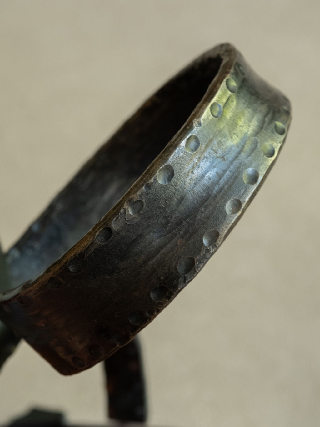 Detail view of the looped wrought iron base showing punched marks, hammered surface texture, dark patina, and visible age wear.