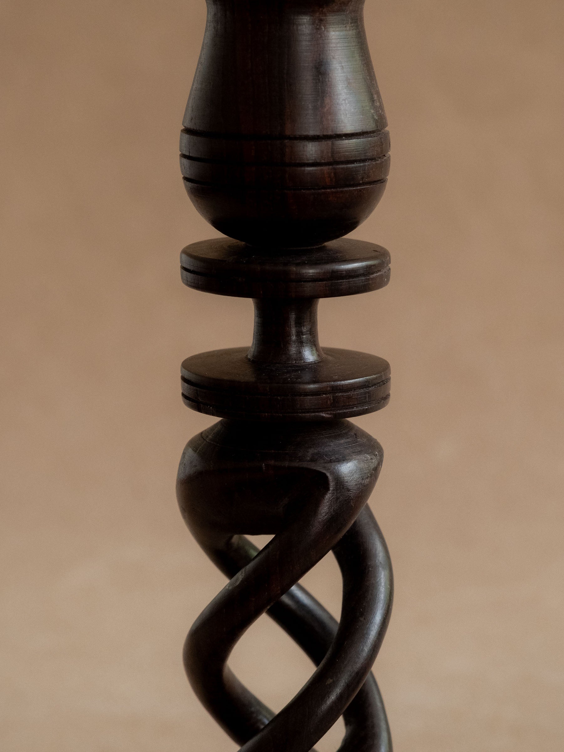 Close view of one ebony candleholder showing the turned upper section and openwork carved body.
