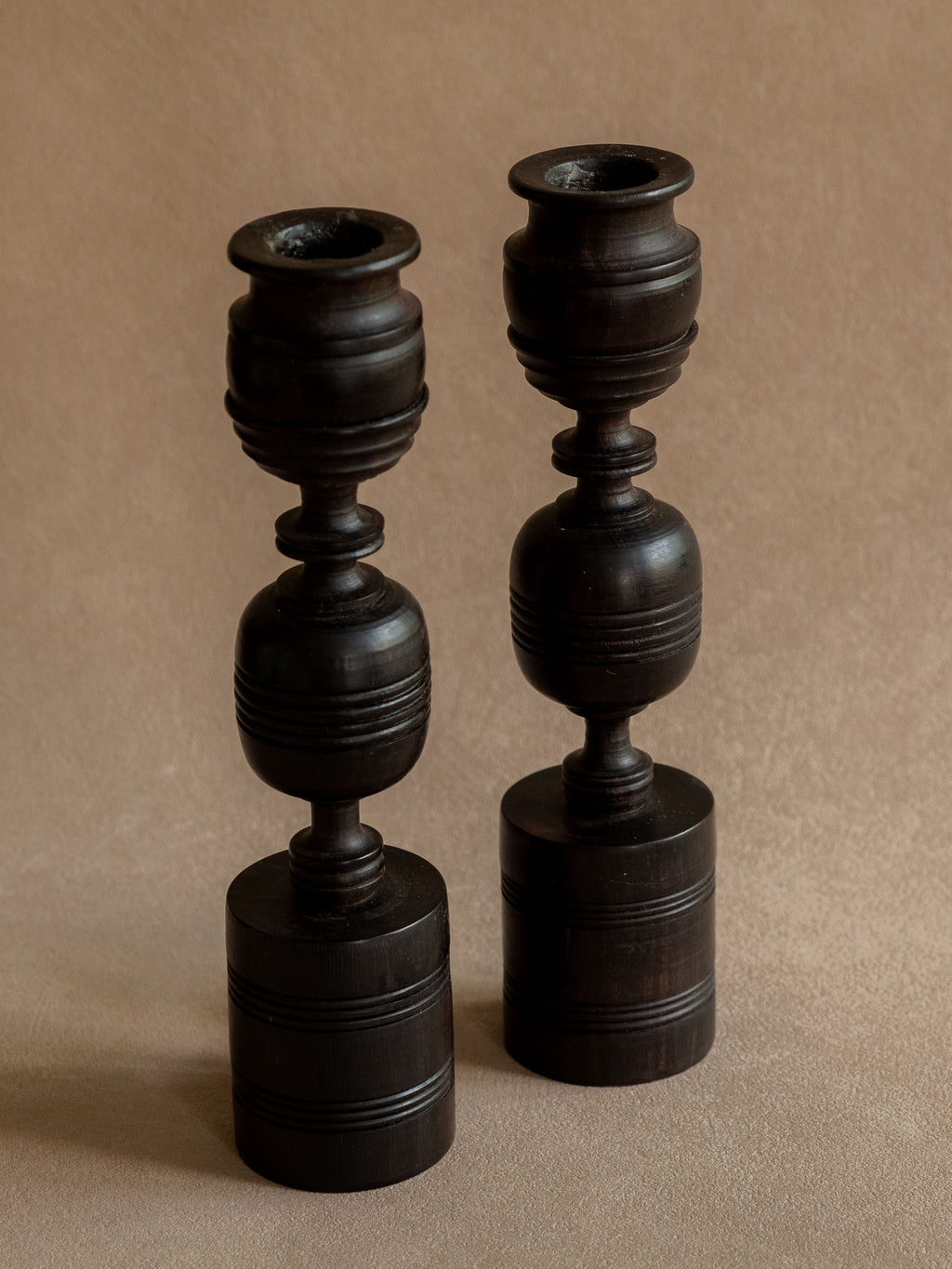 Pair of African turned ebony candleholders shown together from a slight angle against a warm neutral background.