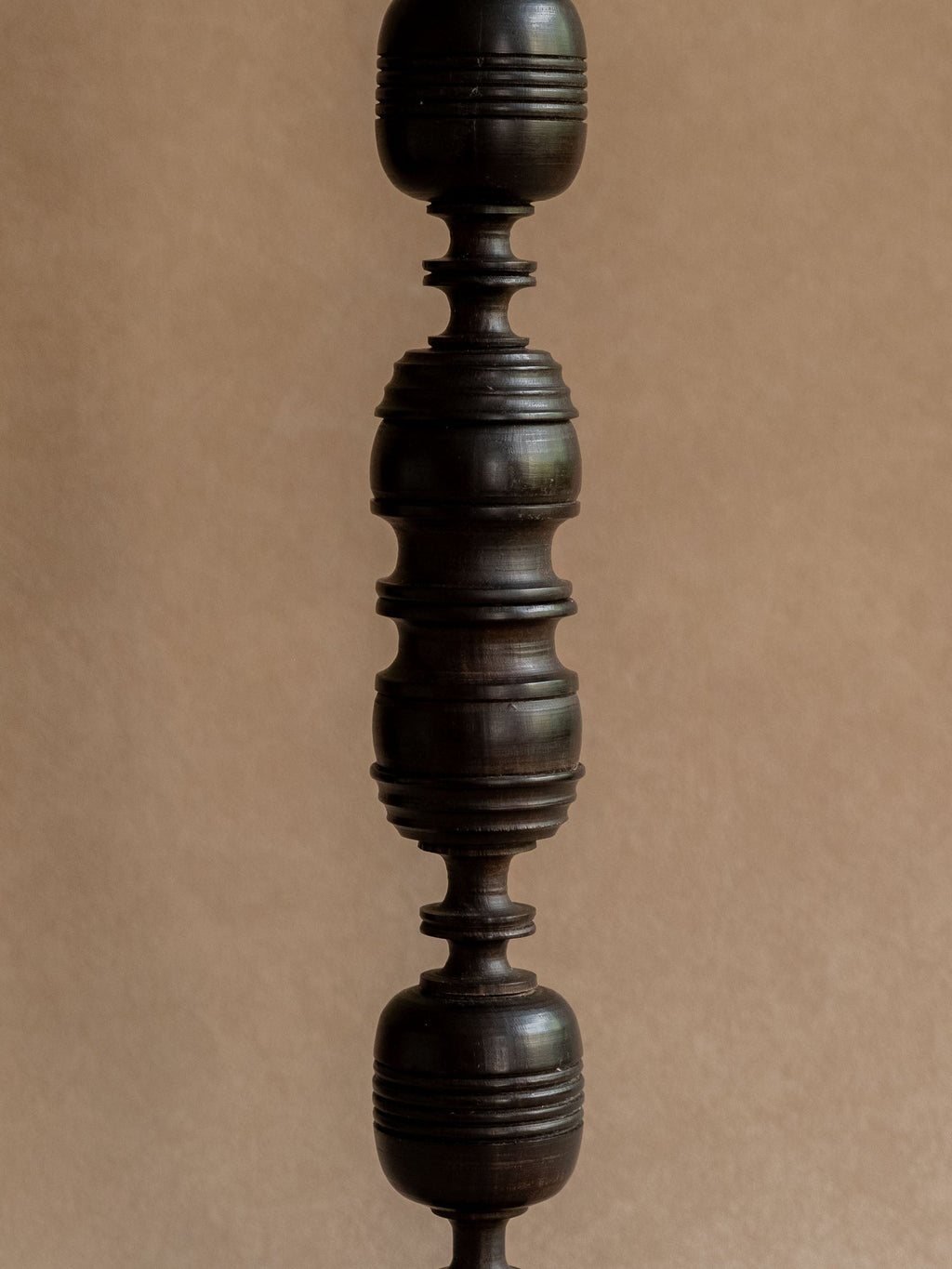 Side detail of a turned ebony candleholder showing the stacked rounded sections and carved grooves.