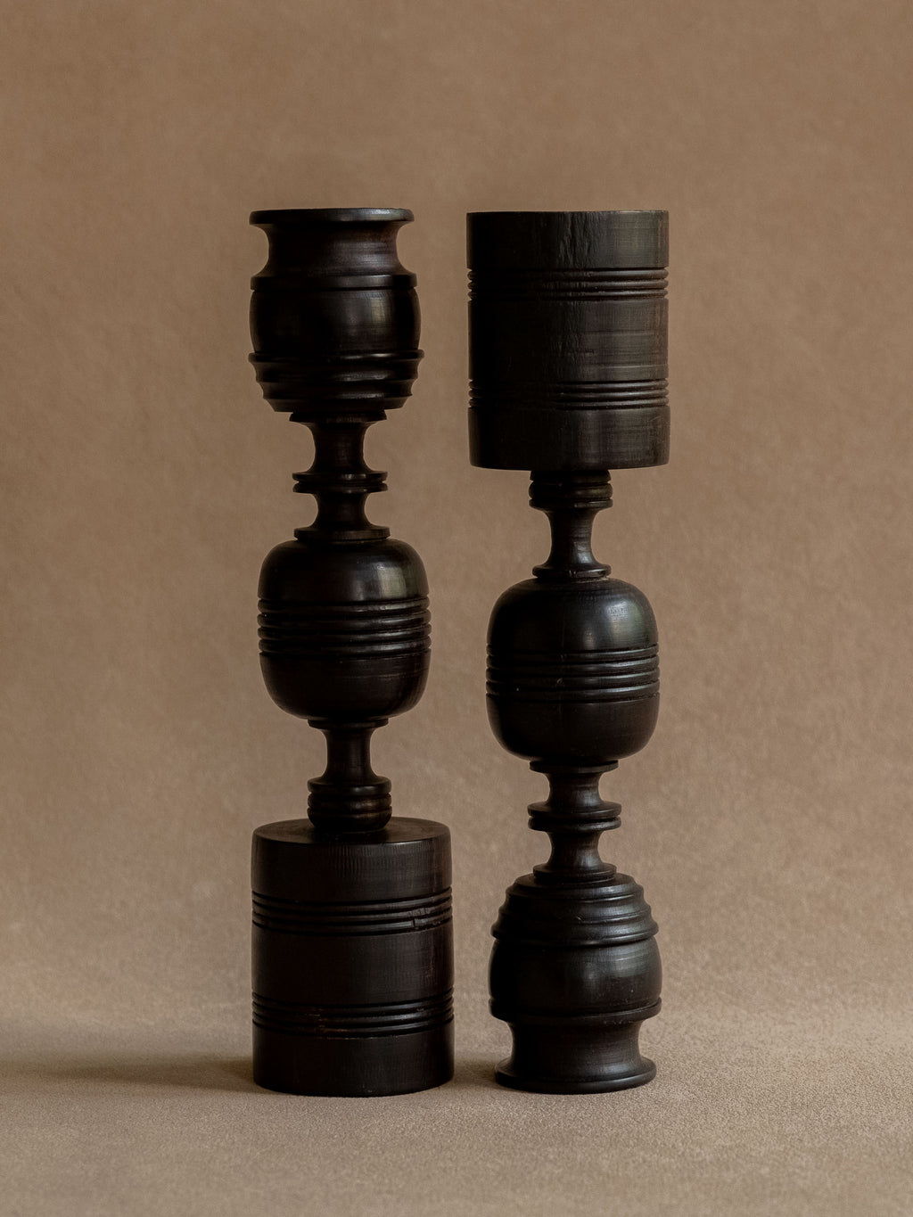Pair of turned ebony candleholders shown in reversed positions to compare their related but individual forms.