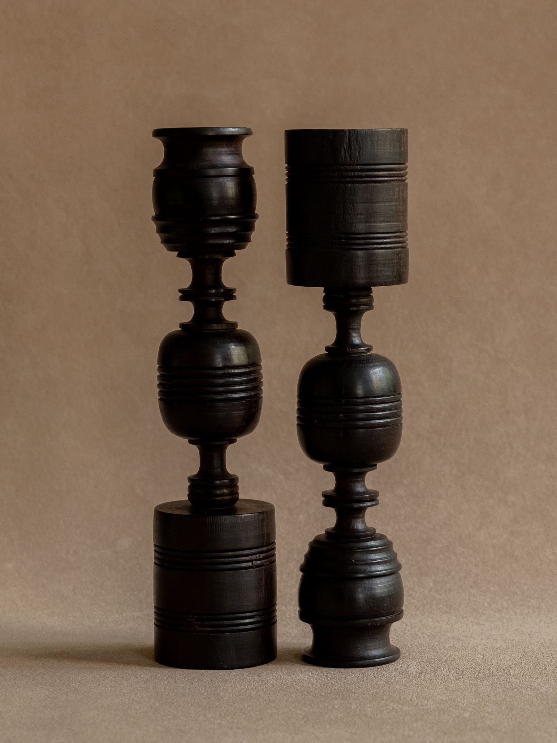 Pair of turned ebony candleholders shown in reversed positions to compare their related but individual forms.