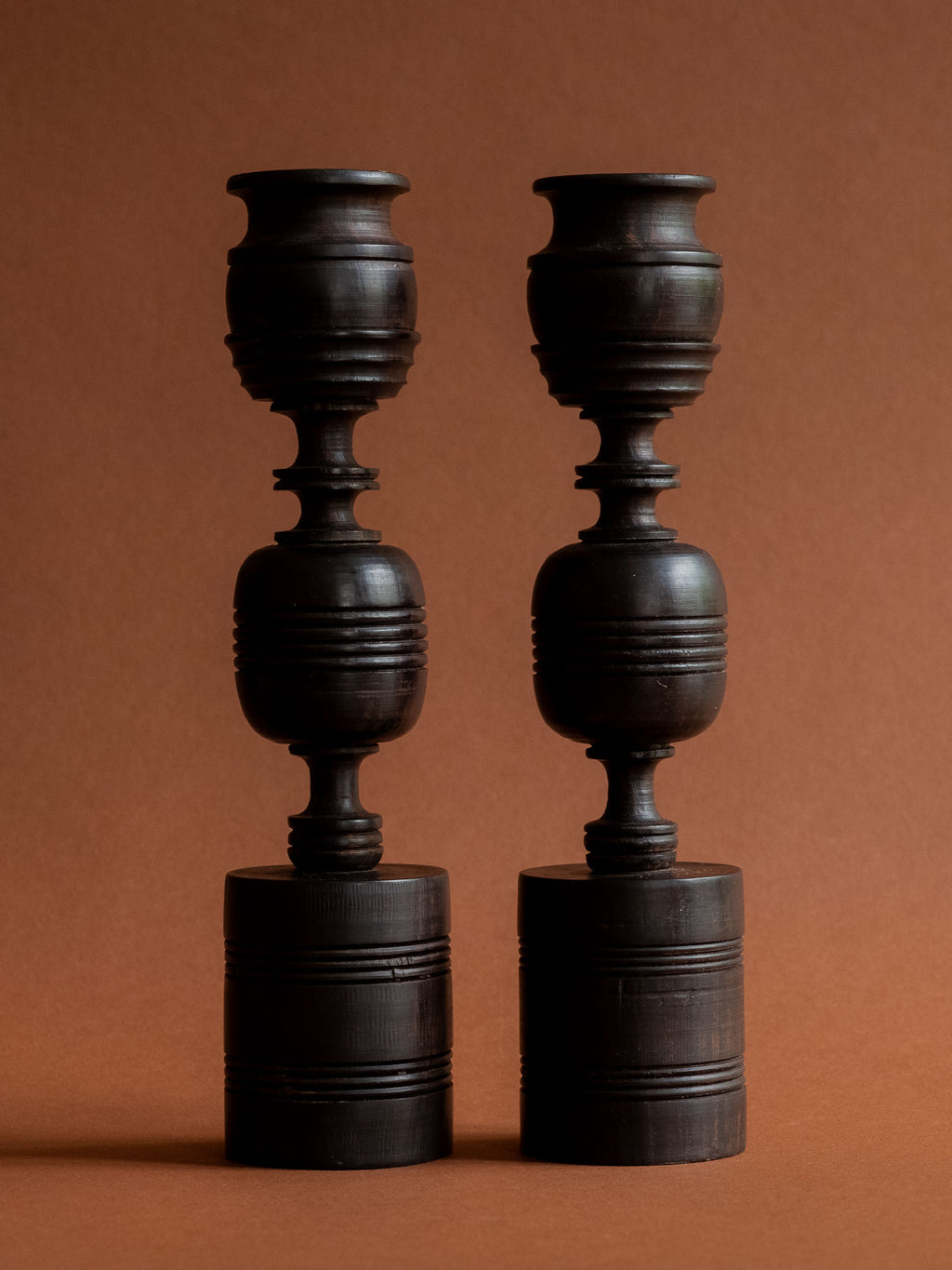 Front view of the pair of dark ebony candleholders against a warm reddish background.